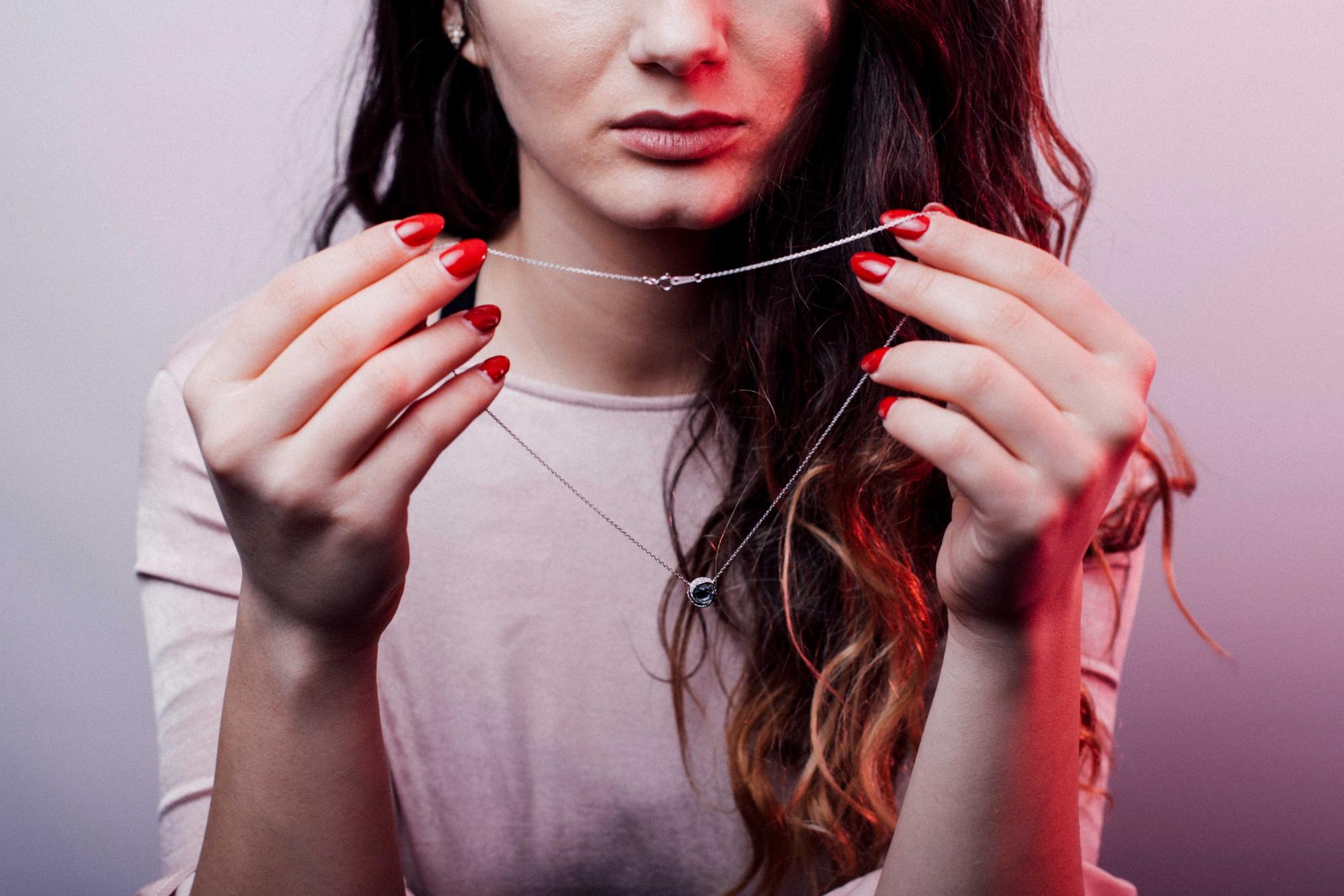 A model holds a necklace from Revival Jewelry while wearing a off-white top.