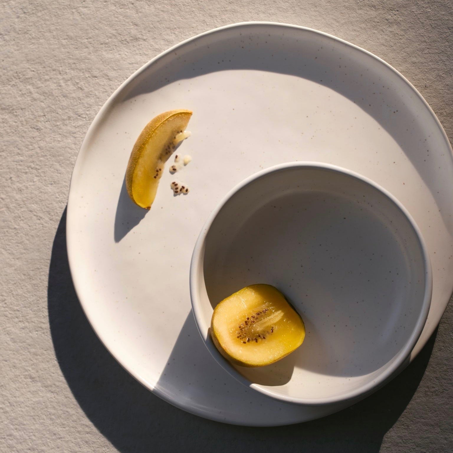 A speckle white plate and bowl with pieces of kiwi.