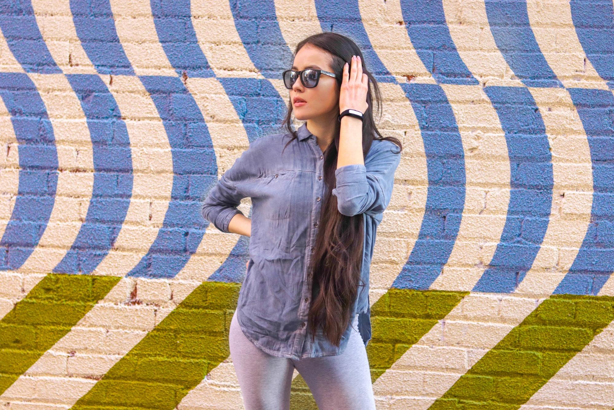 A model wears a HabitAware Keen bracelet in front of a painted mural wall. 
