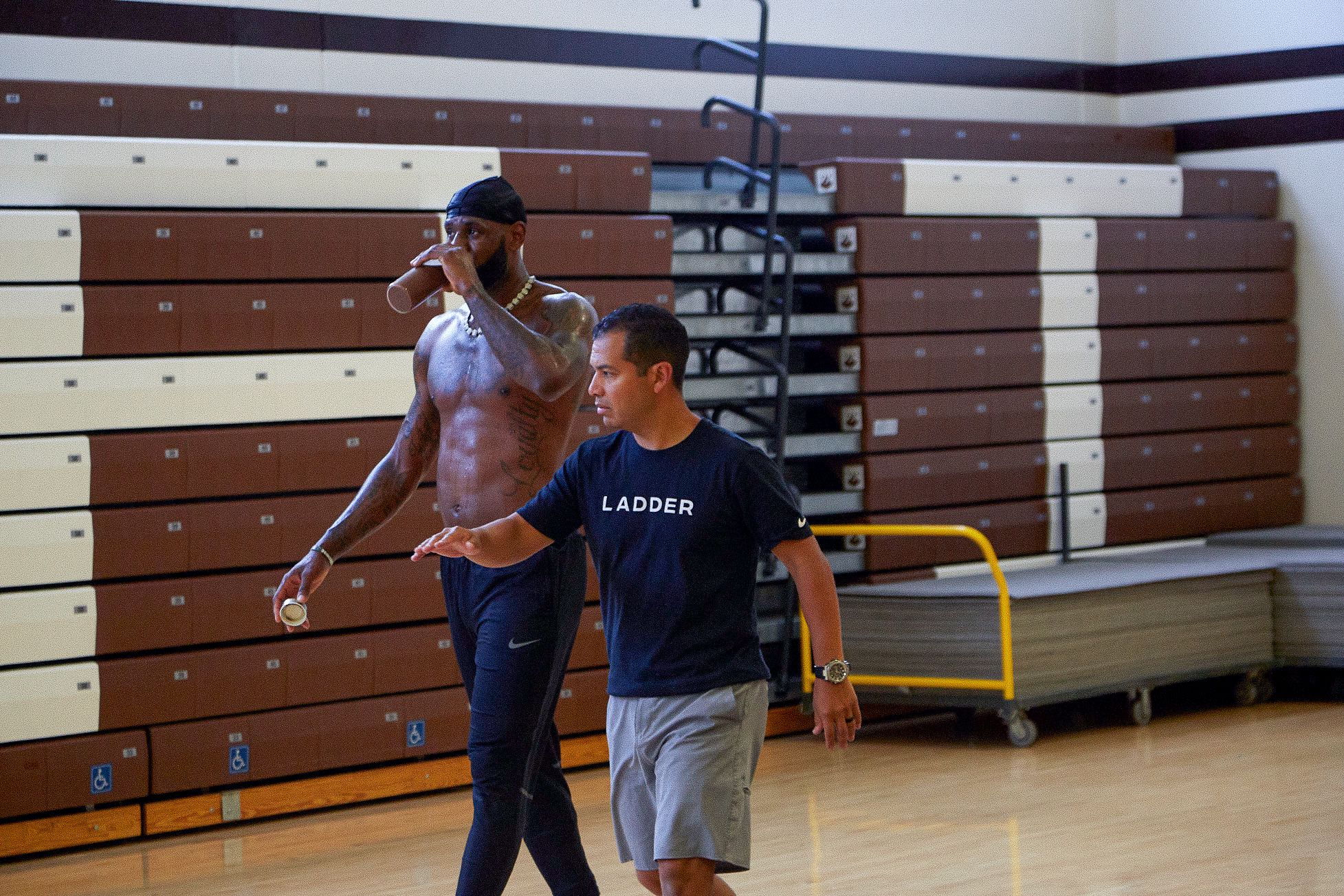 Lebron James drinking a nutrition supplement along with a trainer in a t-shirt that has the “Ladder” logo. 