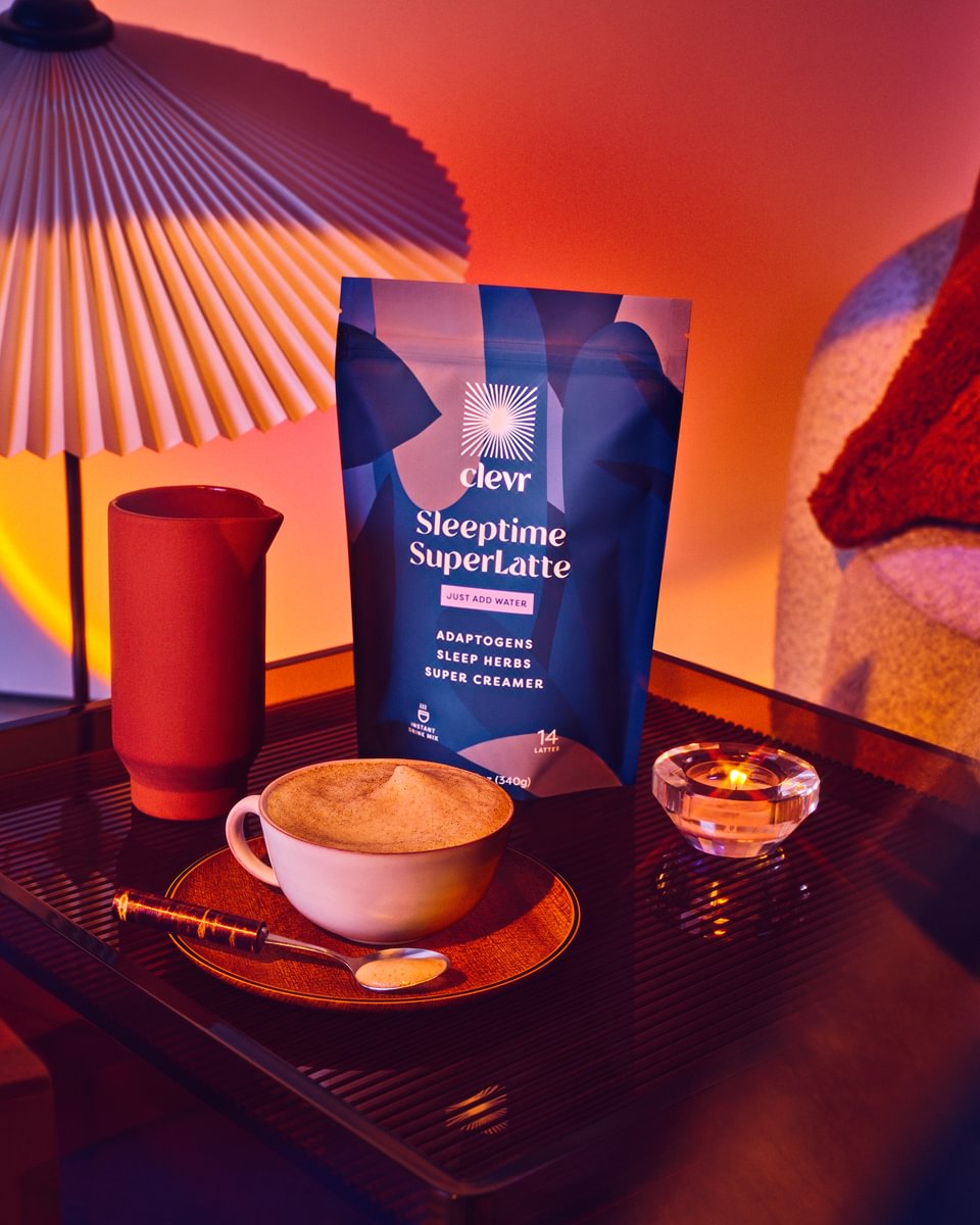 Clevr Blends’ Sleeptime SuperLatte standing beside a lamp, a candle, a glass, and a cup full of the blended beverage. 
