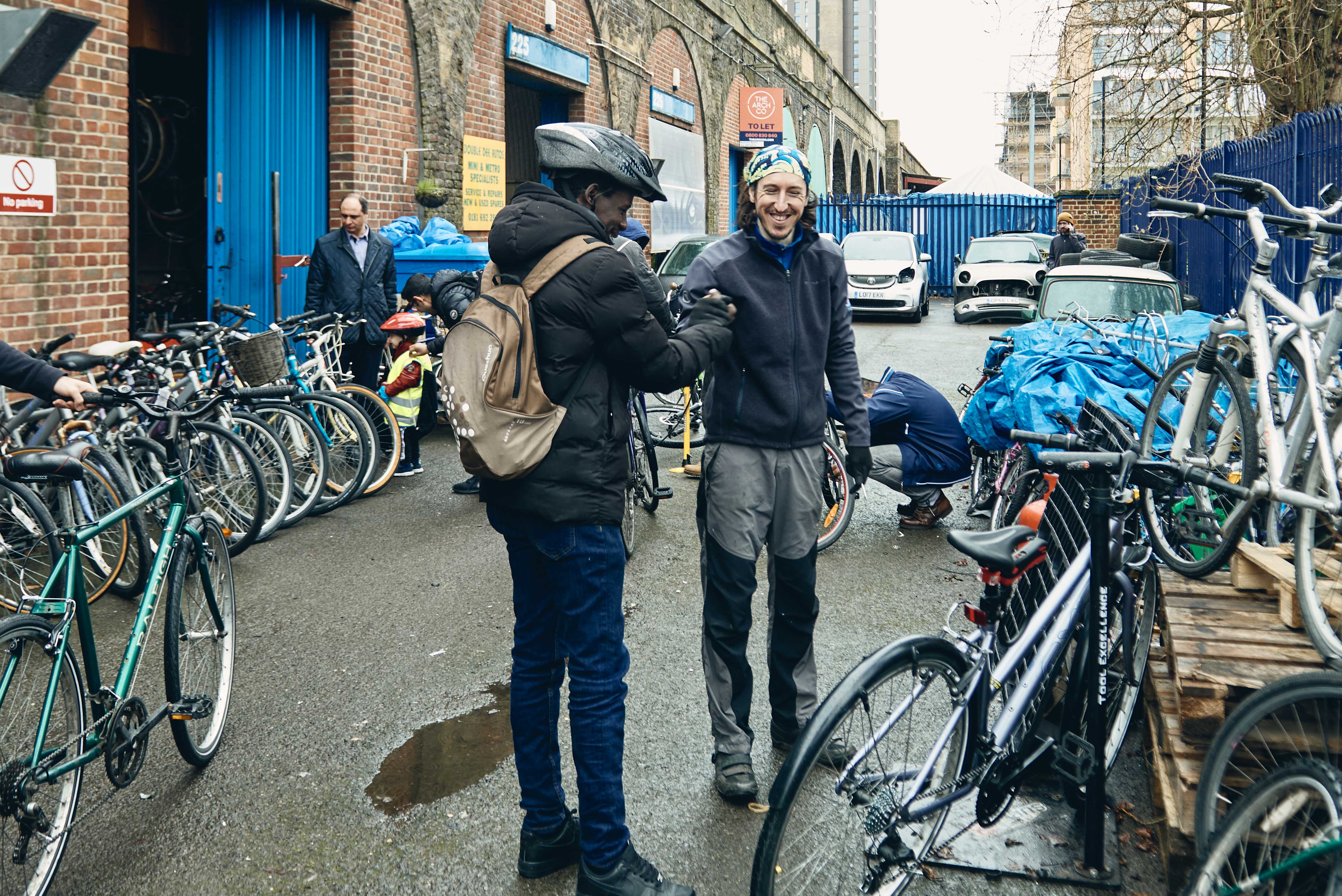 A Mechanic and cyclist greet each other outside of the shop of The Bike Project. 