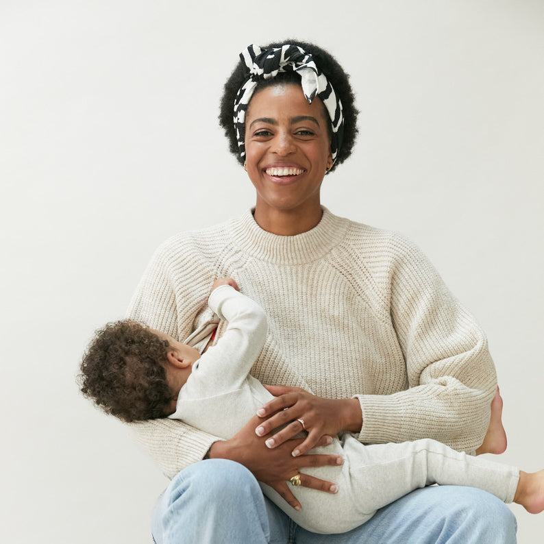 A mom wearing a Tajinebanane sweater while breastfeeding her baby. 