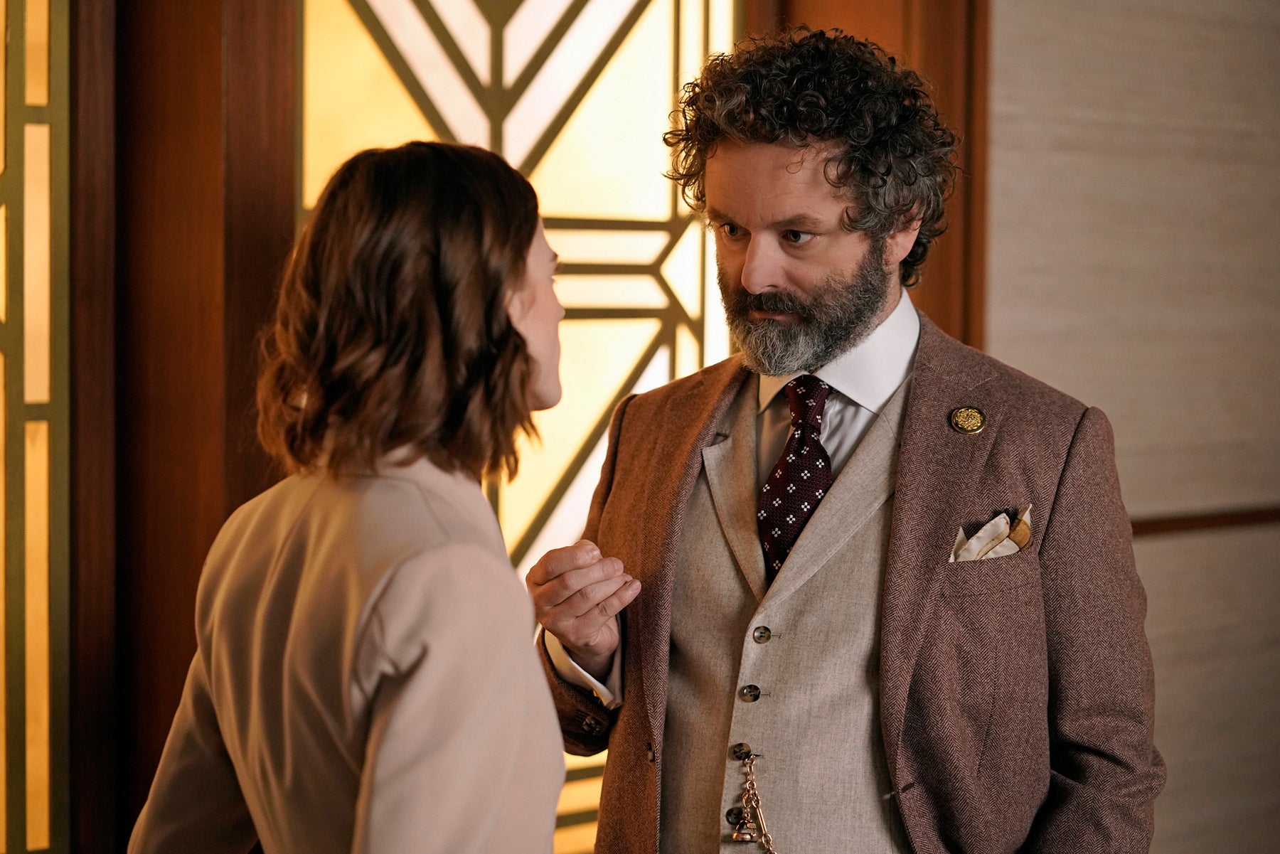 Roland, wearing a three-piece suit, talks to Maia Rindell outside of the courtroom doors.