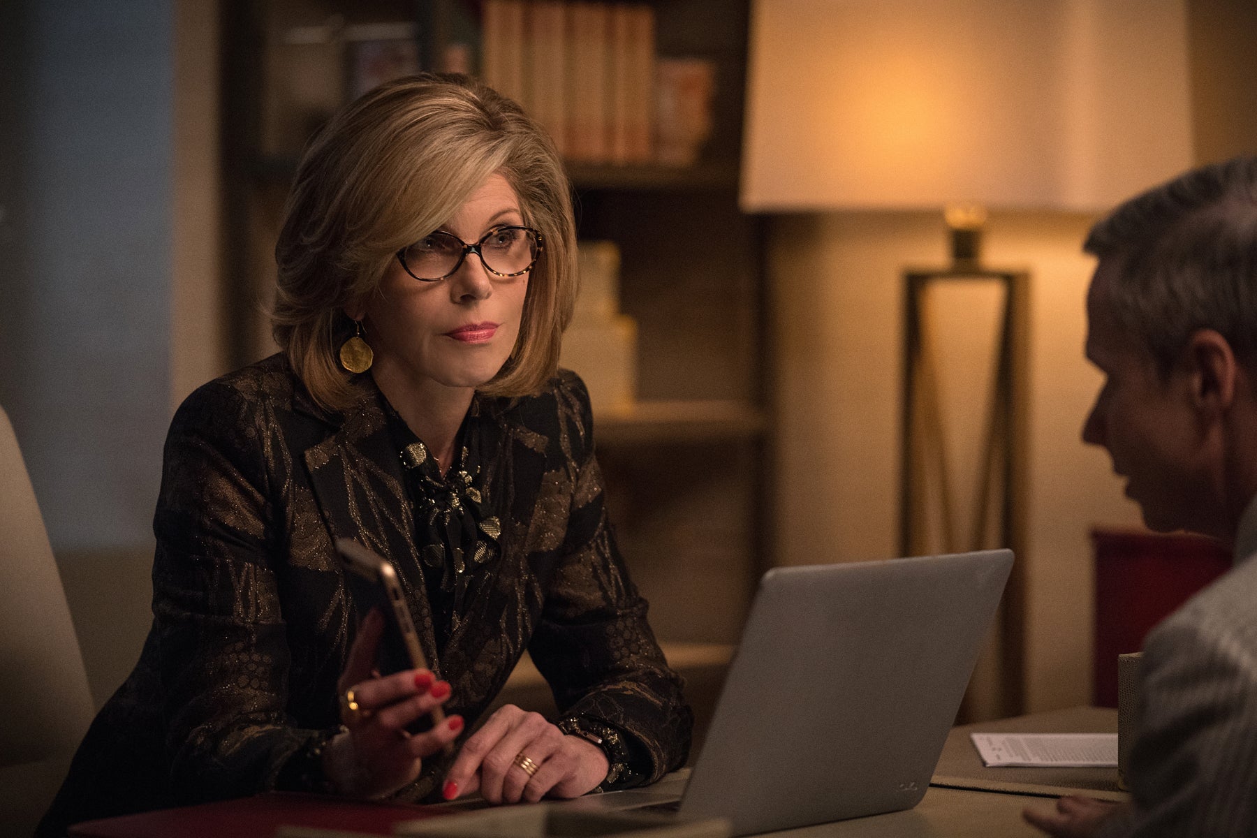 Diane holds her phone up during a meeting with a client, who is sitting across from her desk, as she records their conversation. A laptop is also sitting between them.