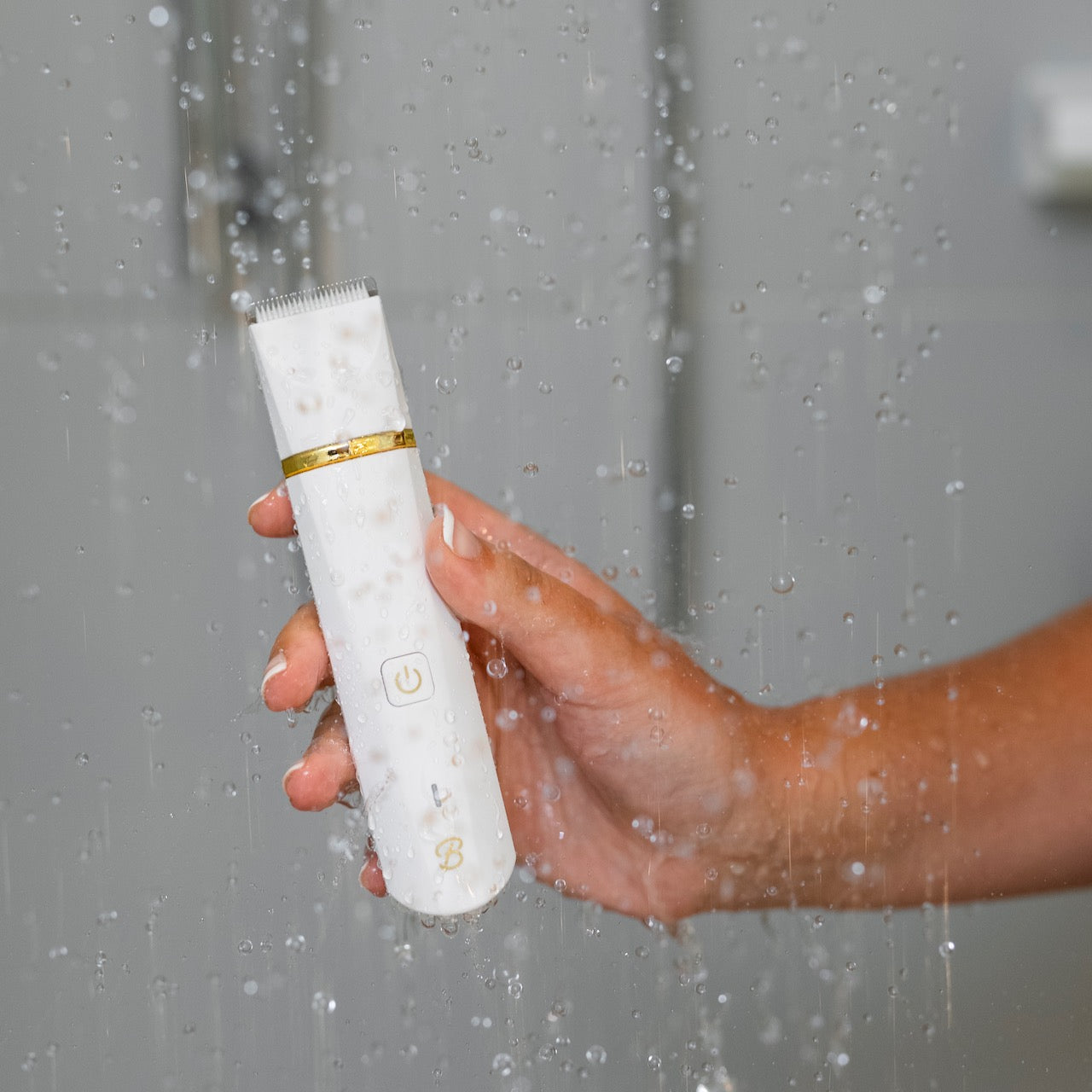 A Bushbalm trimmer held by a hand model in a shower setting.