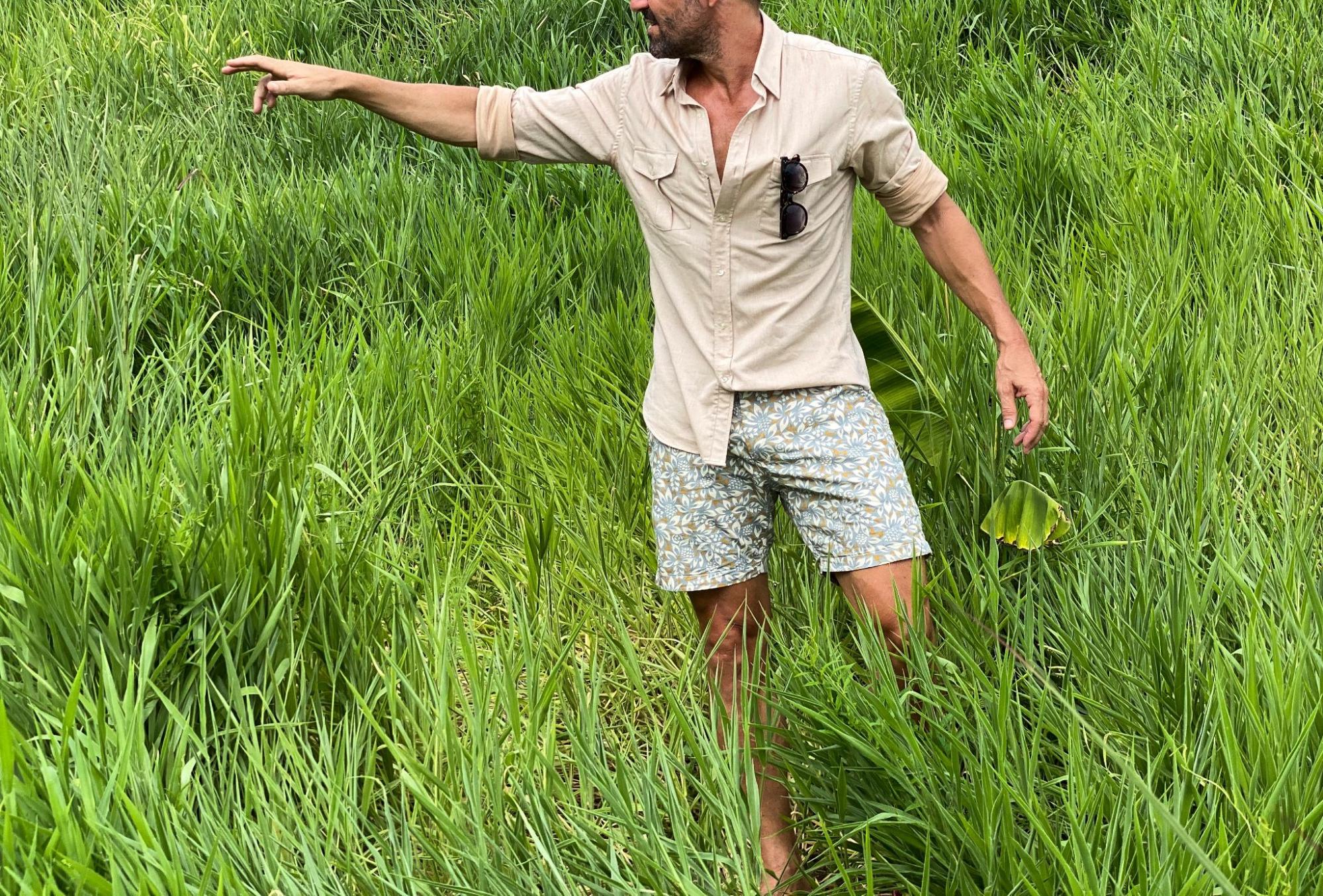 A model in a beige dress shirt by Teddy Strateford and patterned shorts in a grassy field. 