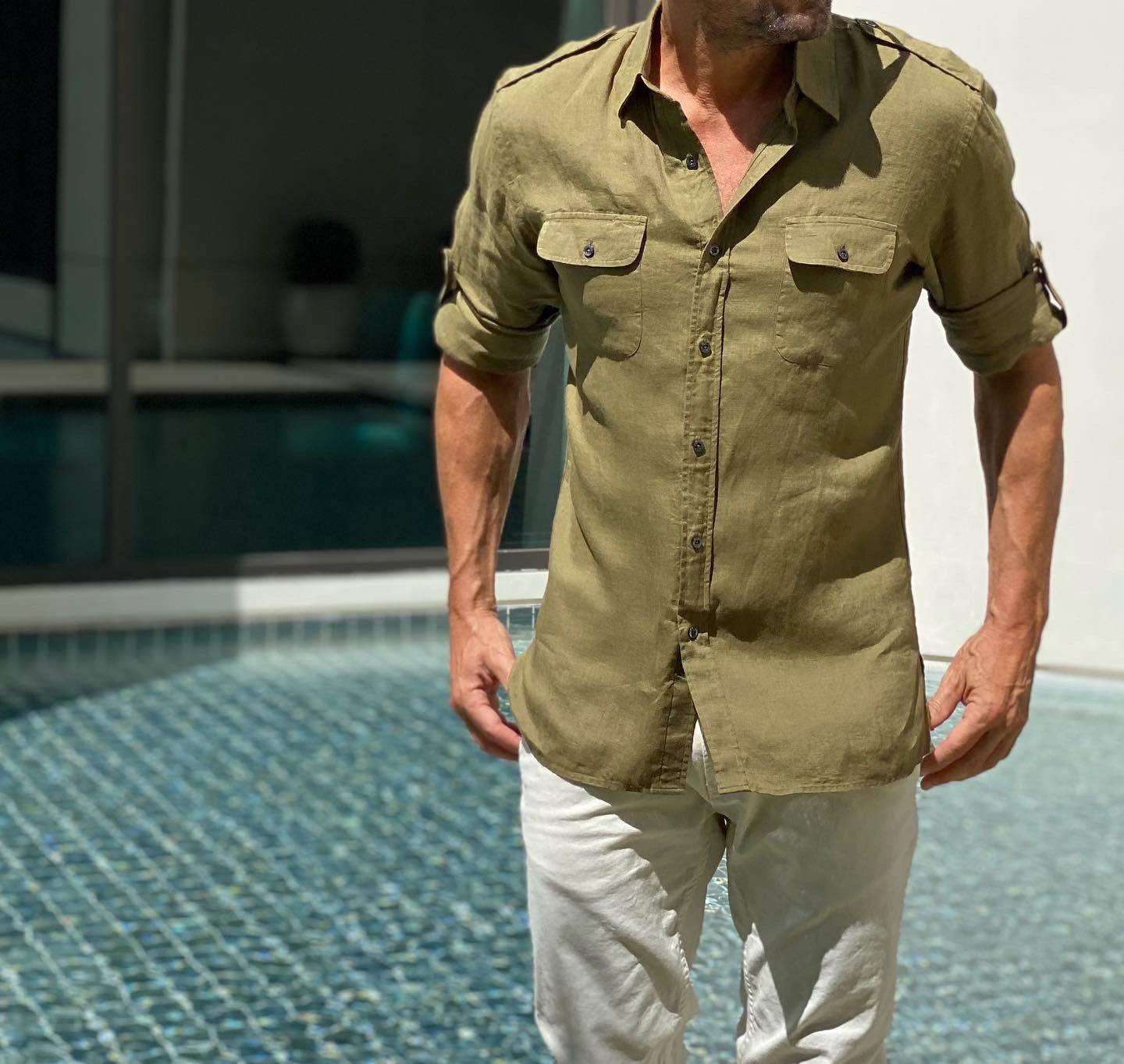 A model wearing an olive coloured dress shirt by Teddy Stratford next to a pool. 