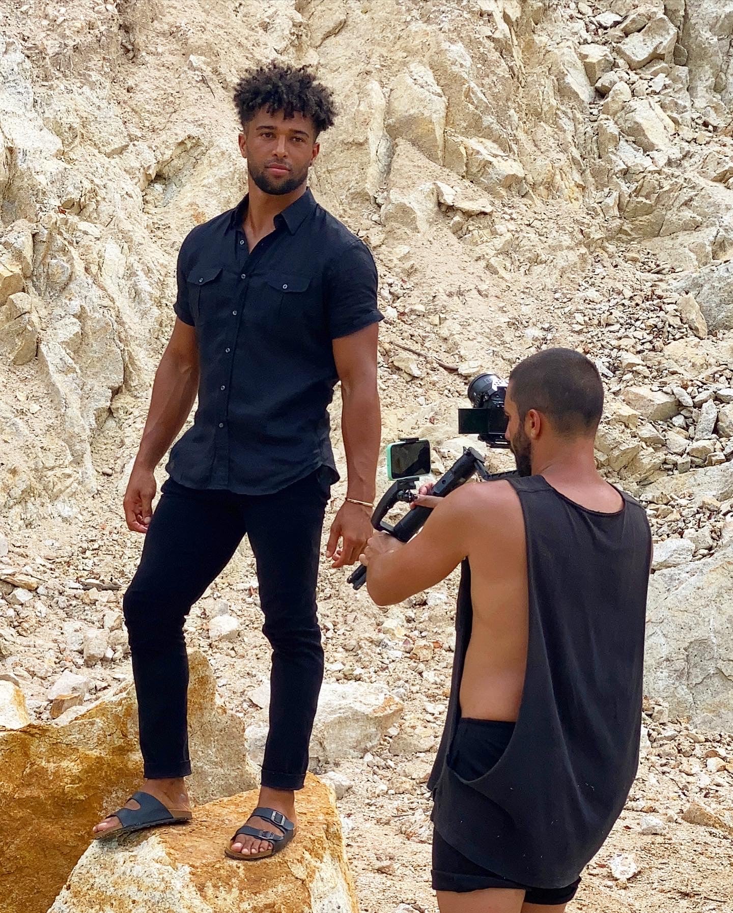 A model in an all black outfit with a videographer filming. 