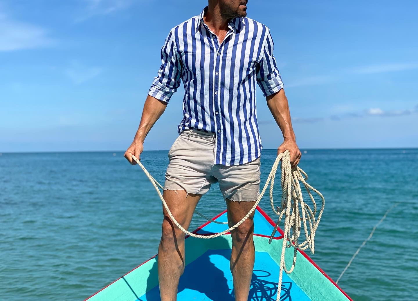 A model in a striped dress shirt by Teddy Stratford and shorts in a boating setting.