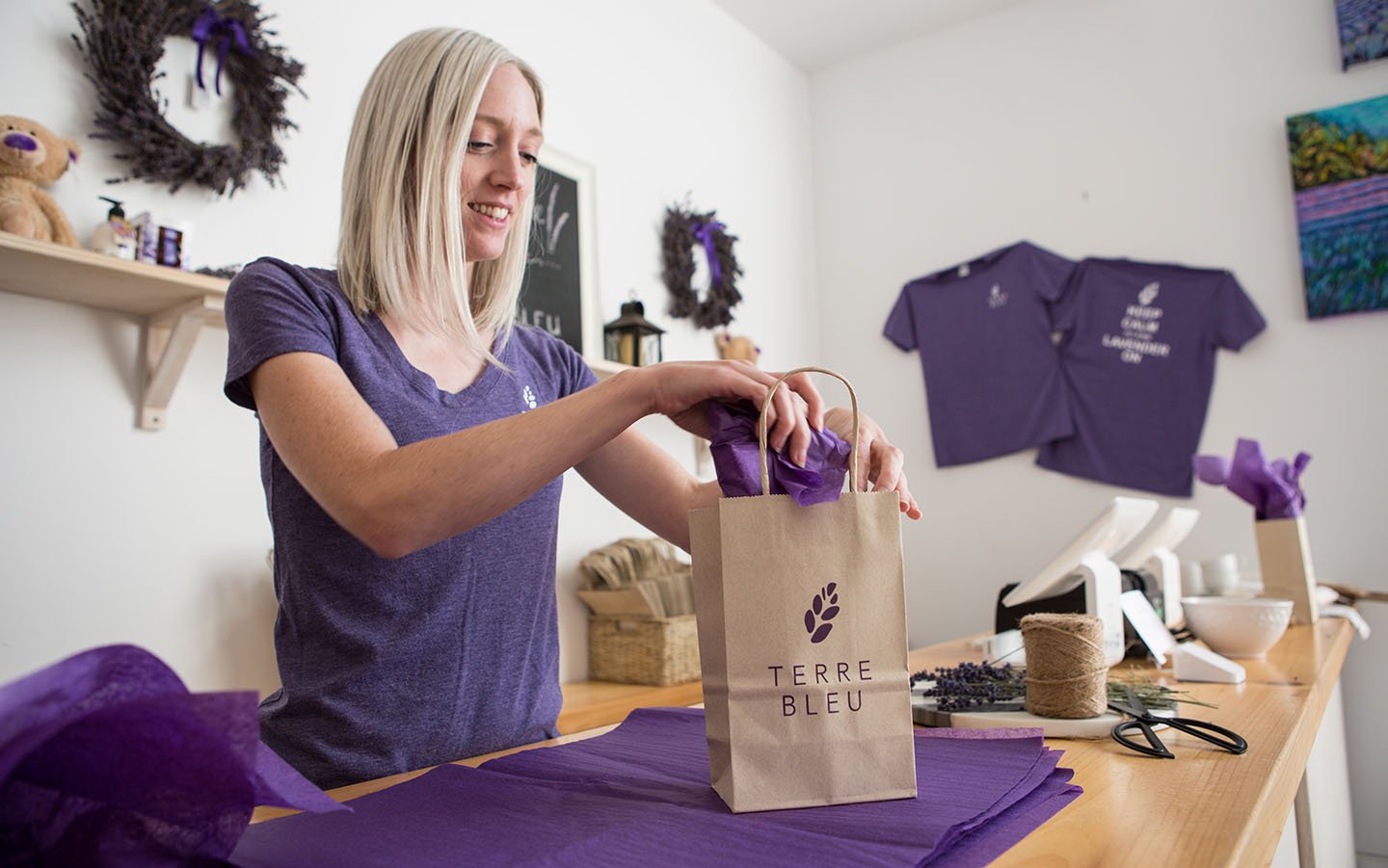 Cashier wearing a lavender shirt bags up a sale at the farm store within Terre Bleu. 