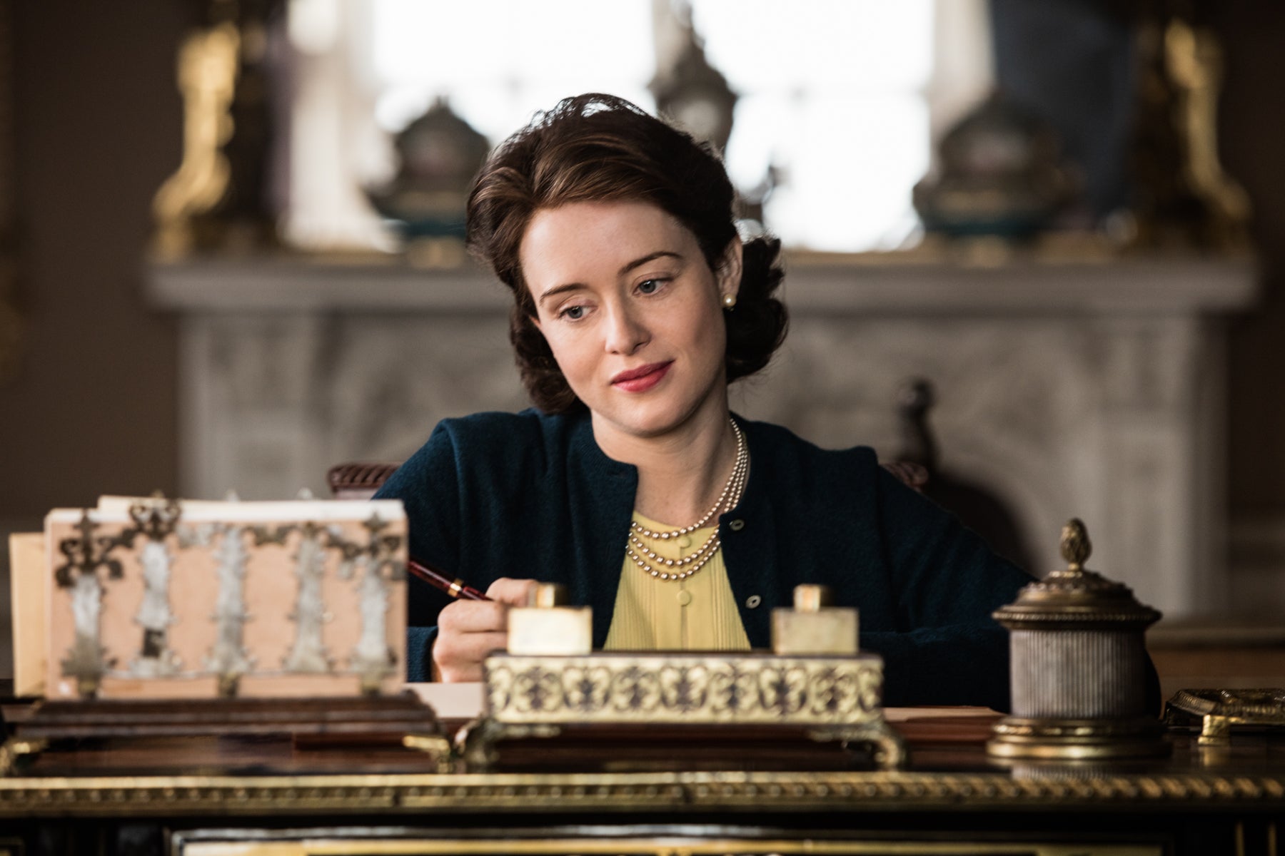 Queen Elizabeth writes at her desk, looking wistful