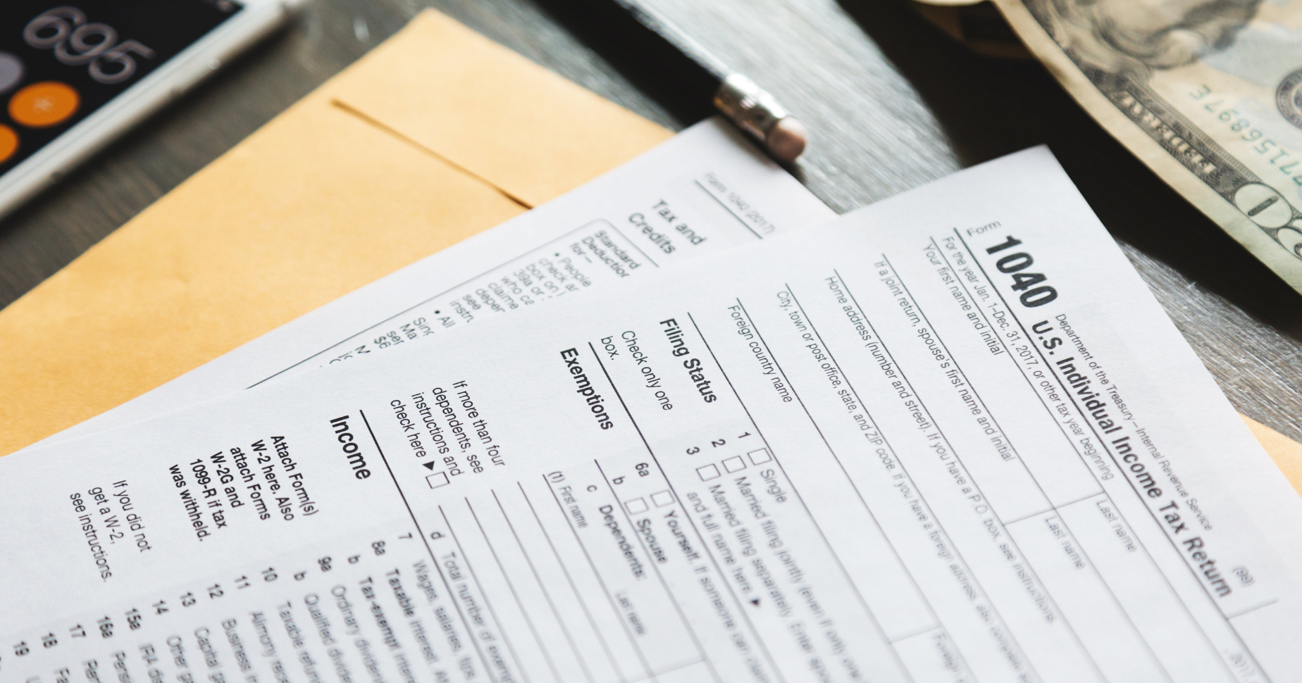 A 1040 tax return form on a table next to a $20 bill and a phone with the calculator app open