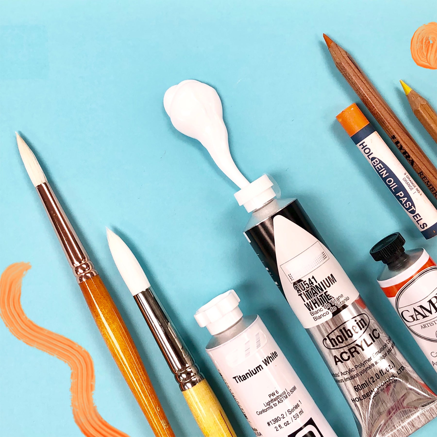 Aerial photograph of paintbrushes and paints placed on top of a bright teal background. 