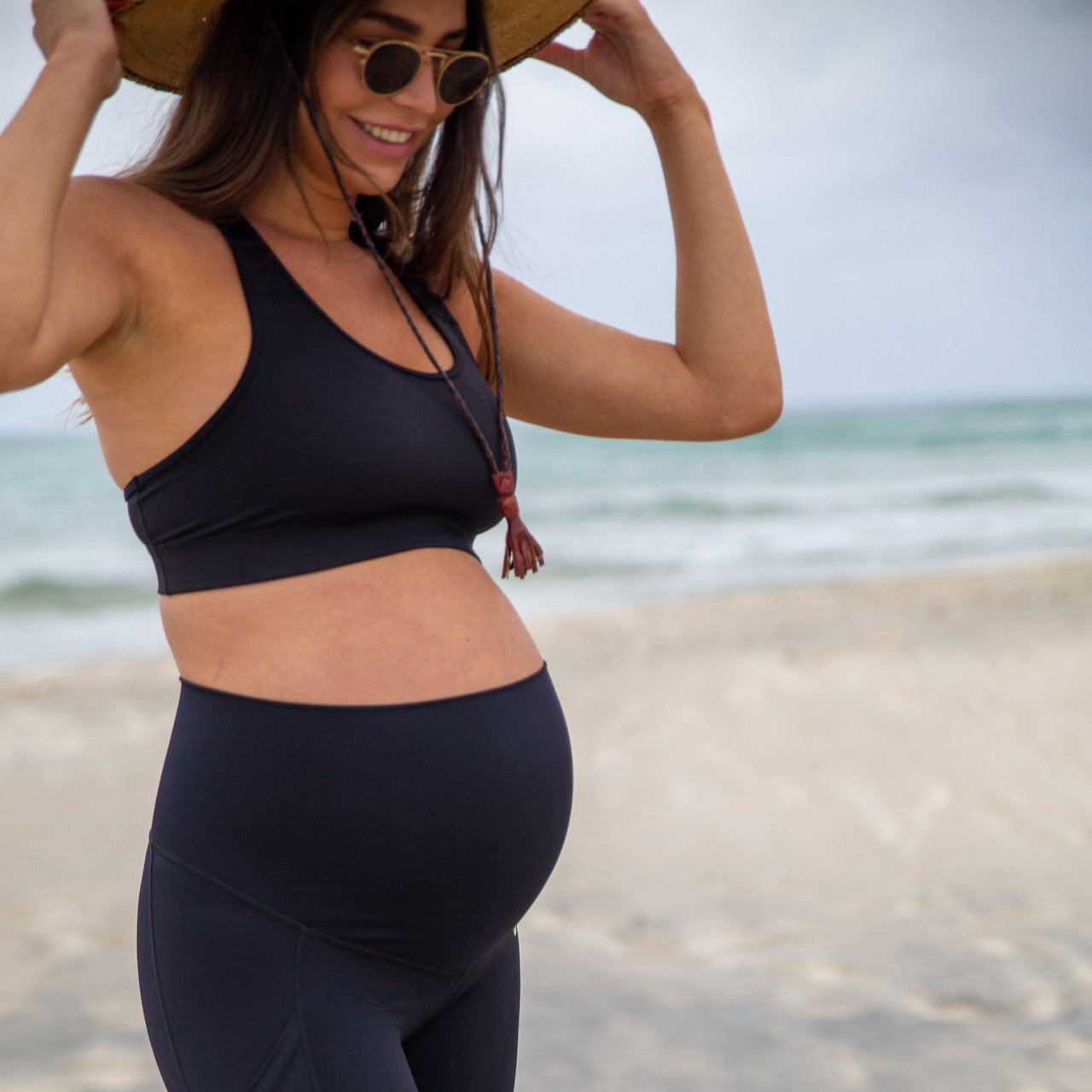 An expecting mom models an outfit from Active Truth backdropped by the beach.