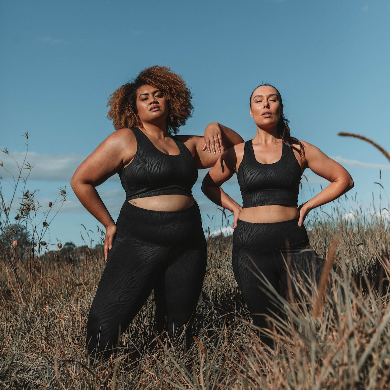 Two models wearing black workout sets from Active Truth in a field setting.