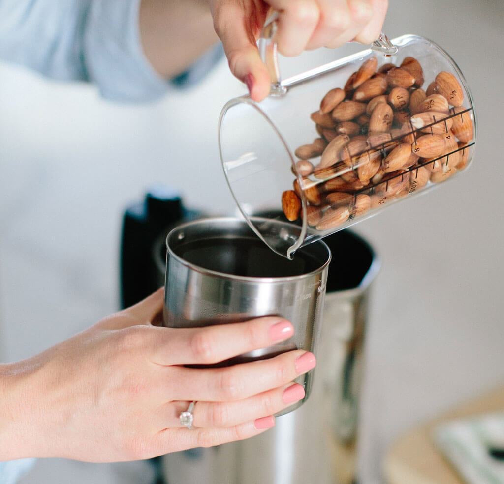 A woman pours almonds into an Almond Cow plant based milk maker