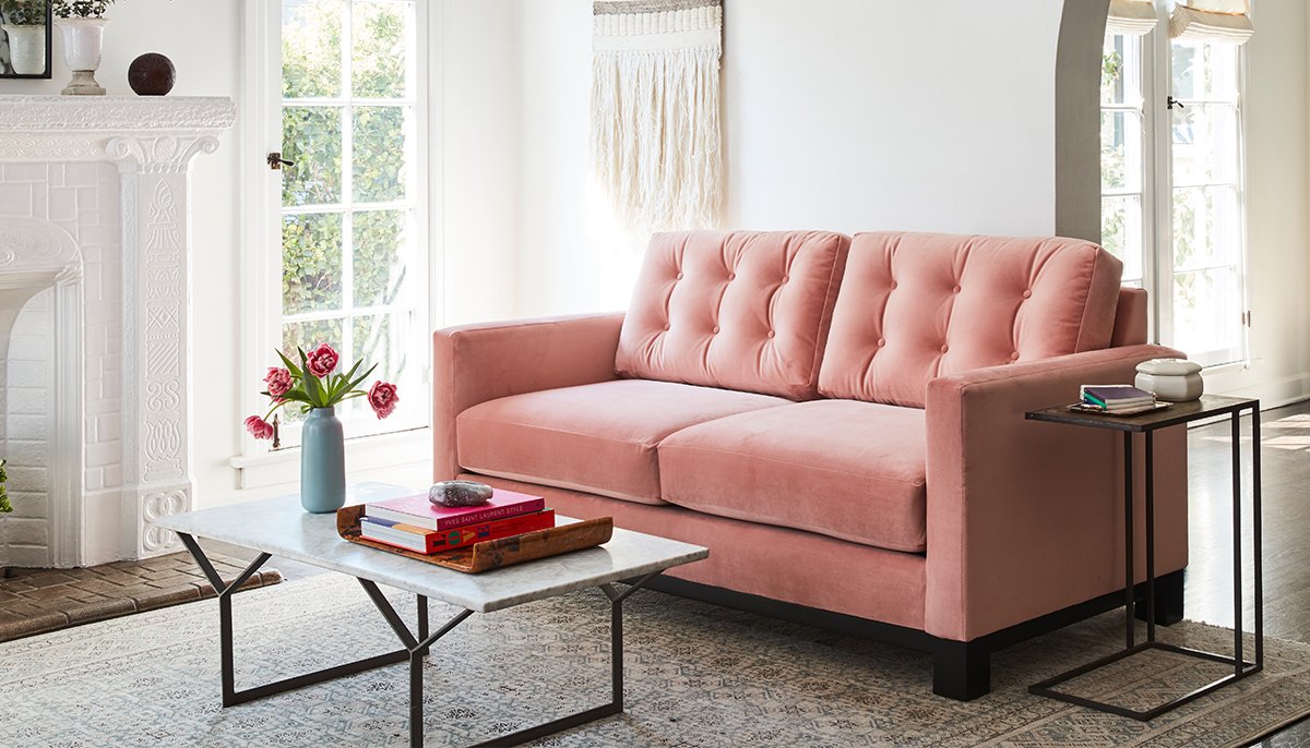 A blush colored loved seat with a marble coffee table in a living room setting. 