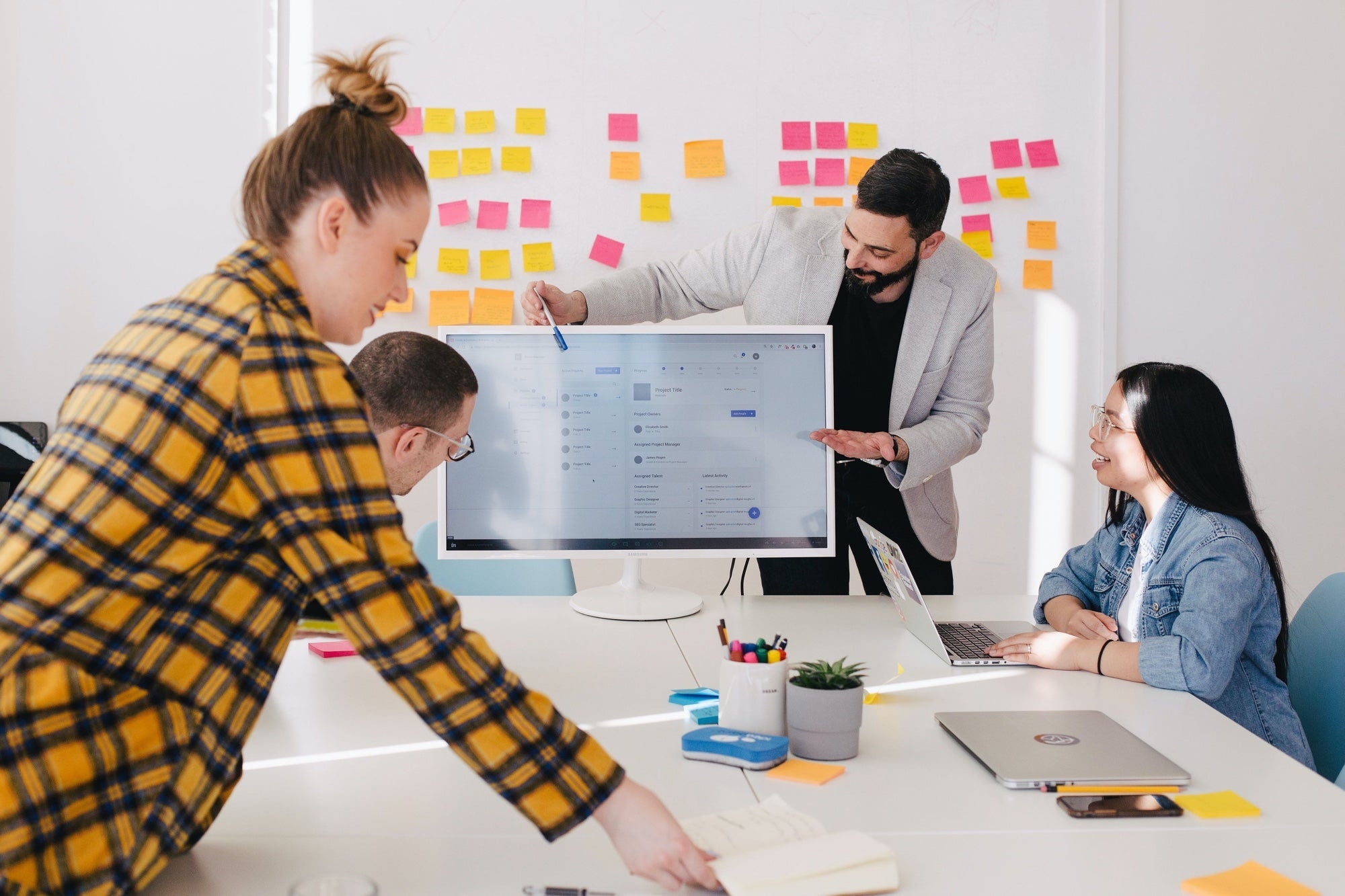 Team of employees sitting around a white table and man pointing at a website on a screen