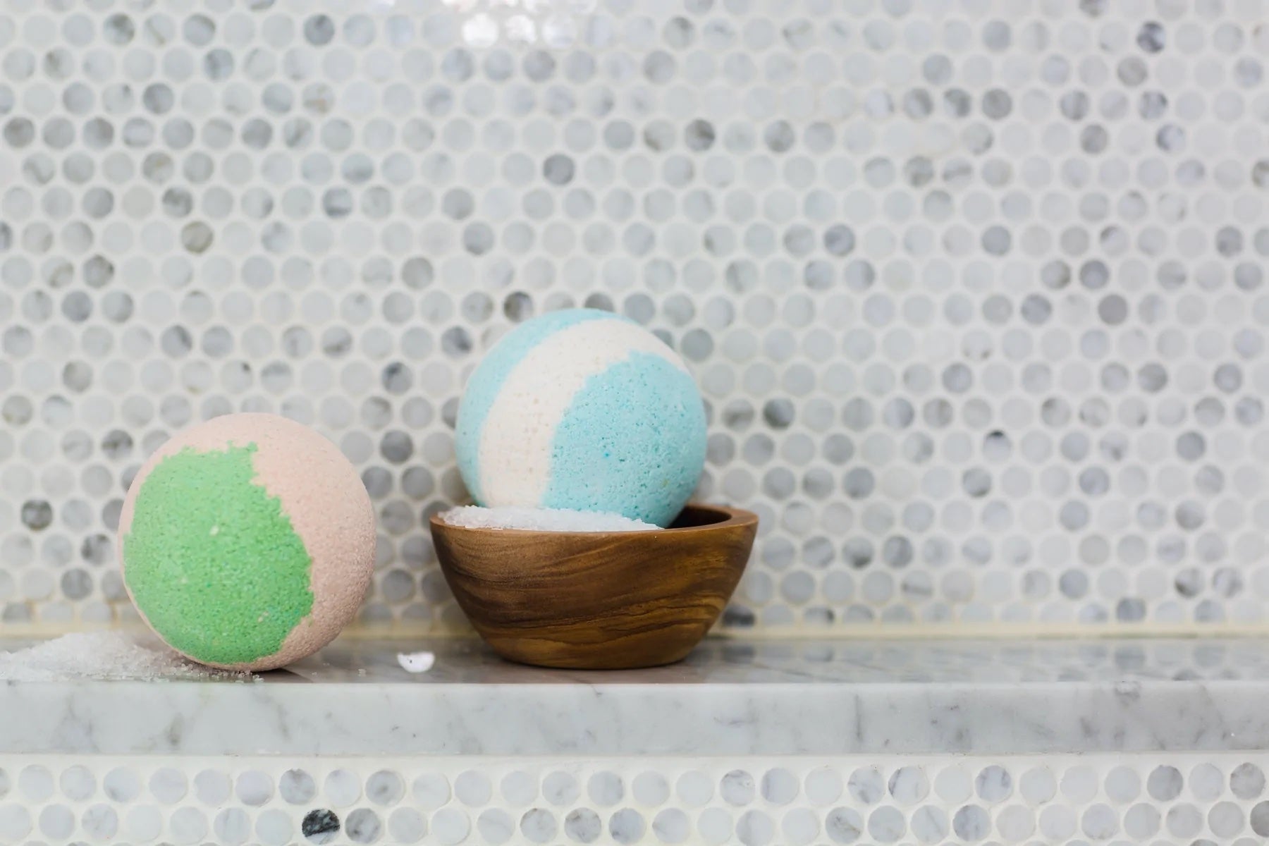 Two handmade bath bombs sit on a shower ledge