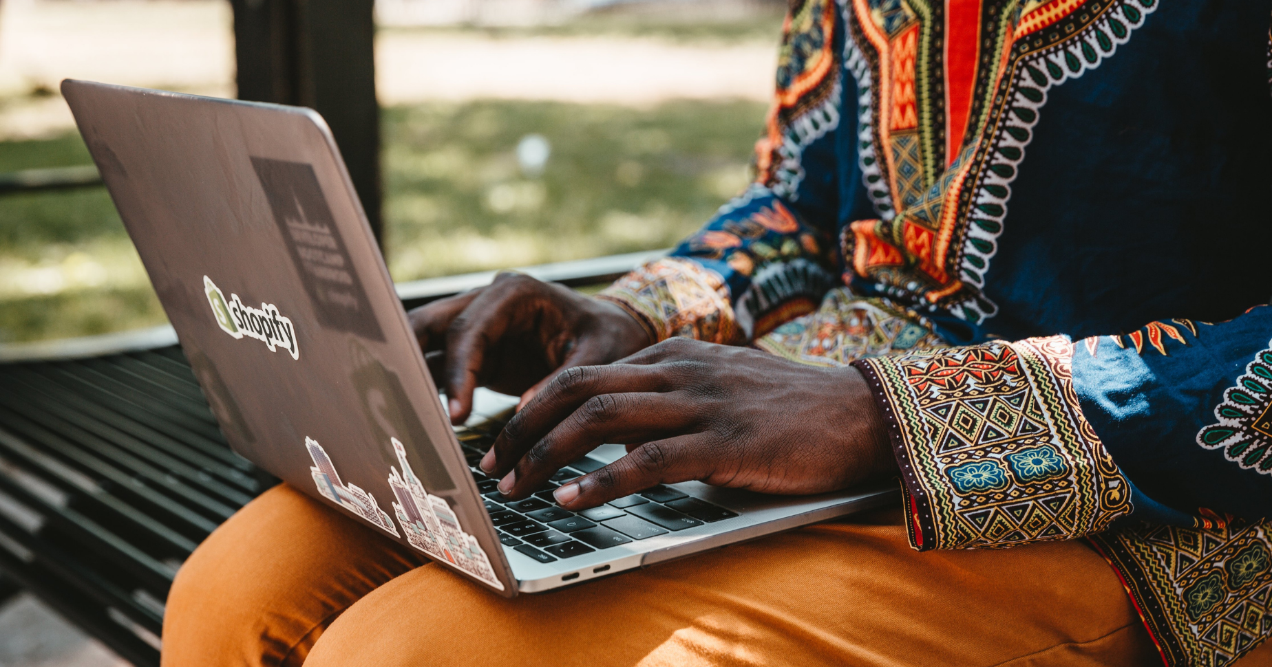 Photograph of a man sitting on a park bench registering a domain name from his laptop