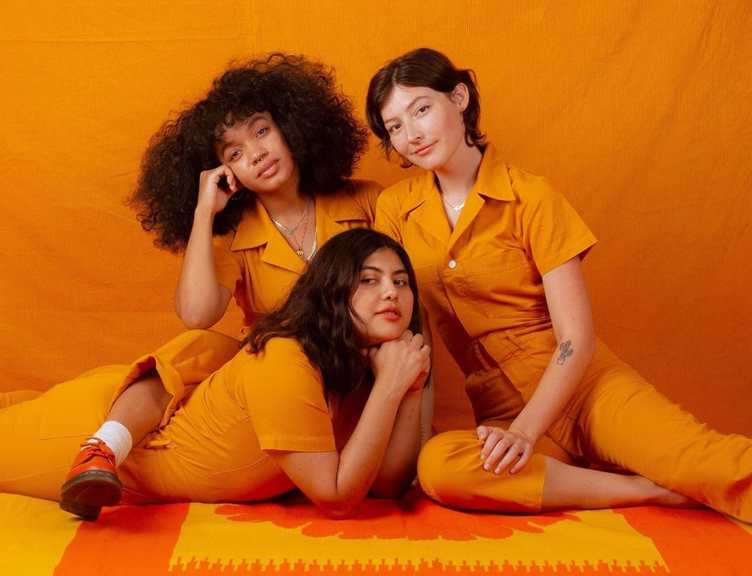 Three models wearing Big Bud Press orange jumpsuits against an orange background