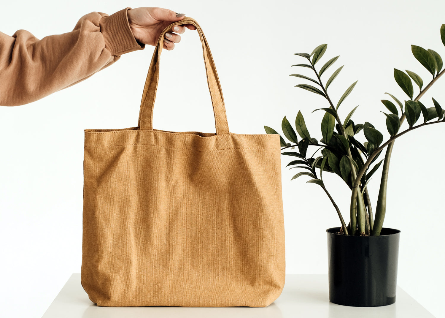 A hand demonstrates the handle of a blank tote bag