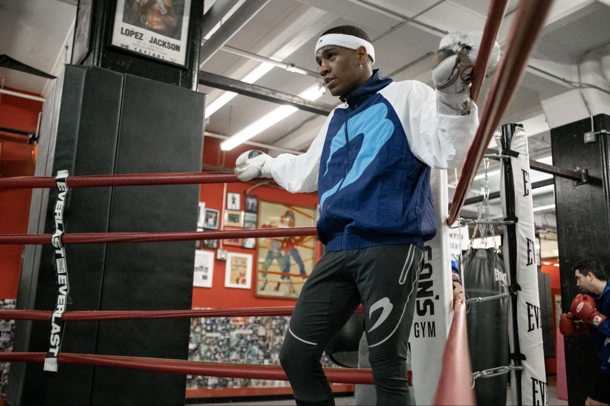 A male boxer in a Boxraw outfit at a corner of a boxing ring. 