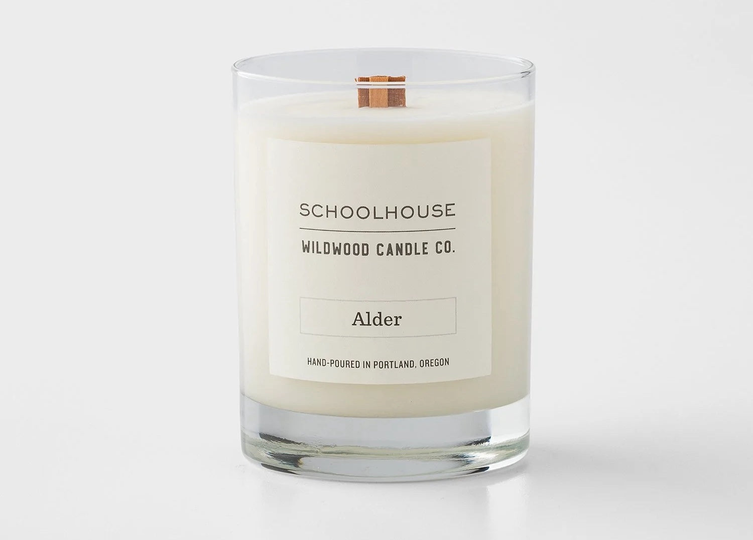 A white candle in a glass jar with a simple white label and wooden wick