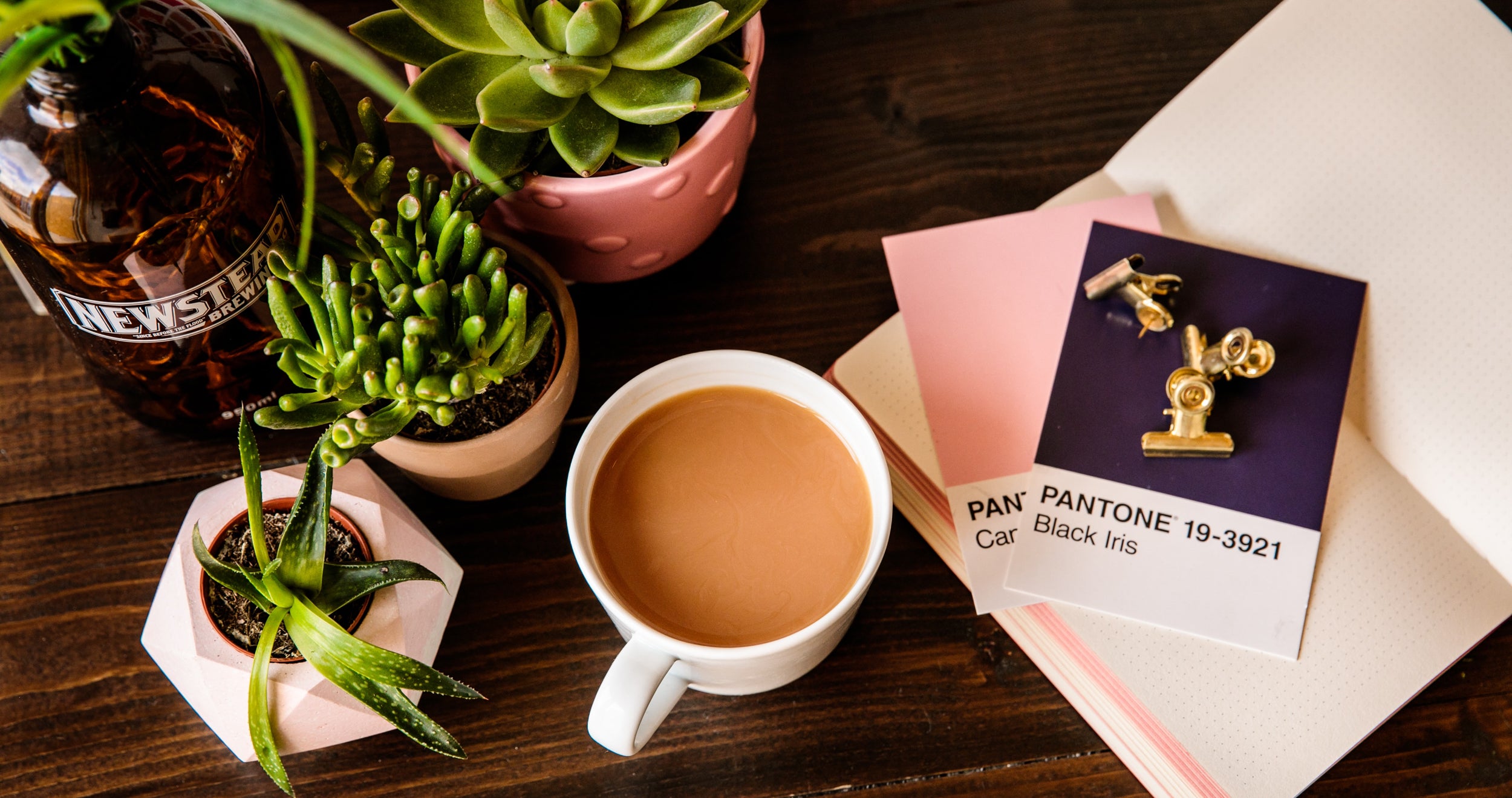 Top view of a desk with a coffee, notebook, plants, and Pantone swatches