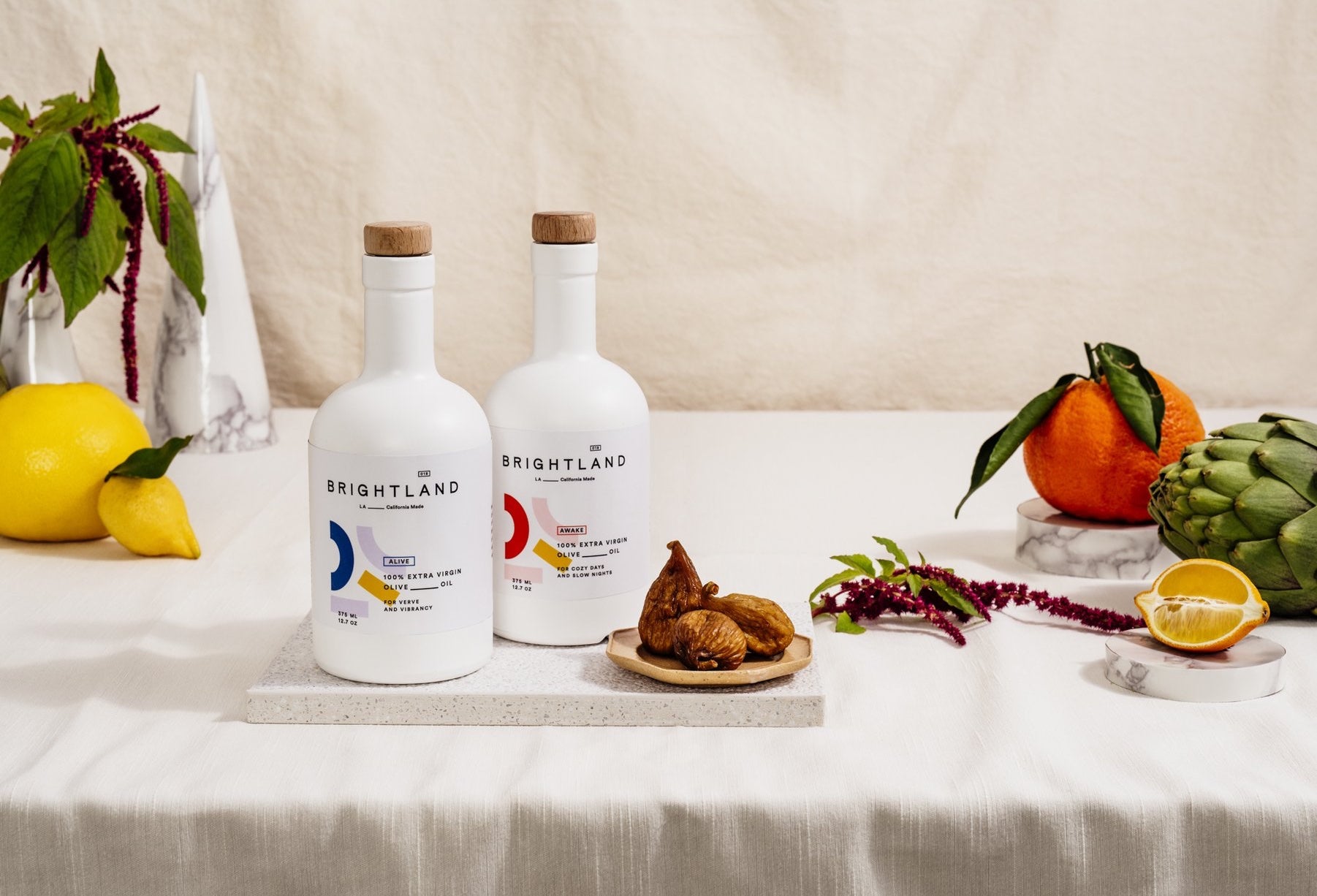 Two bottles of Brightland olive oil sitting on a table staged with food