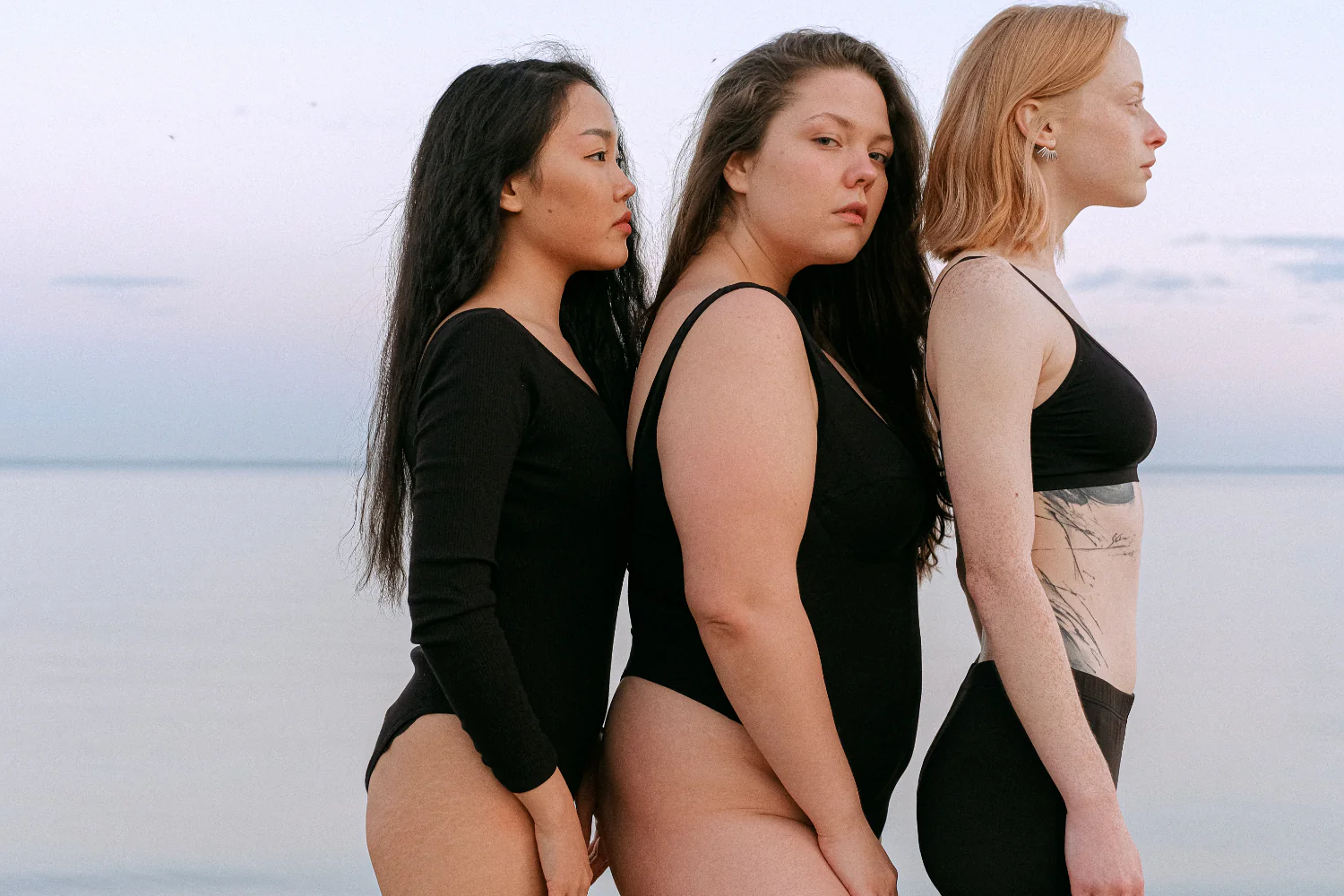 Three women and front to back in a row in front of a lake