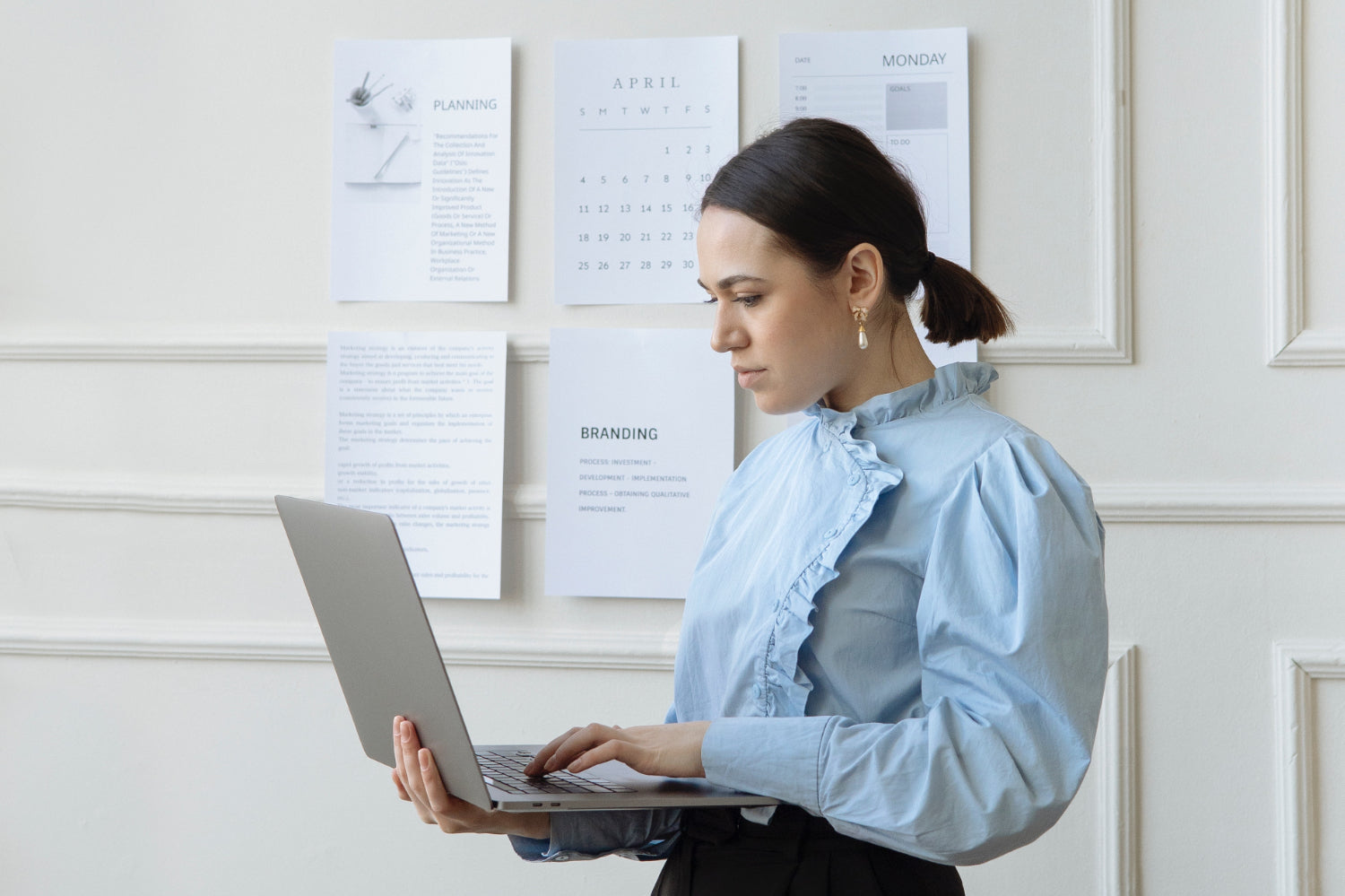 A woman looks at a laptop against a wall covered in business plan documents