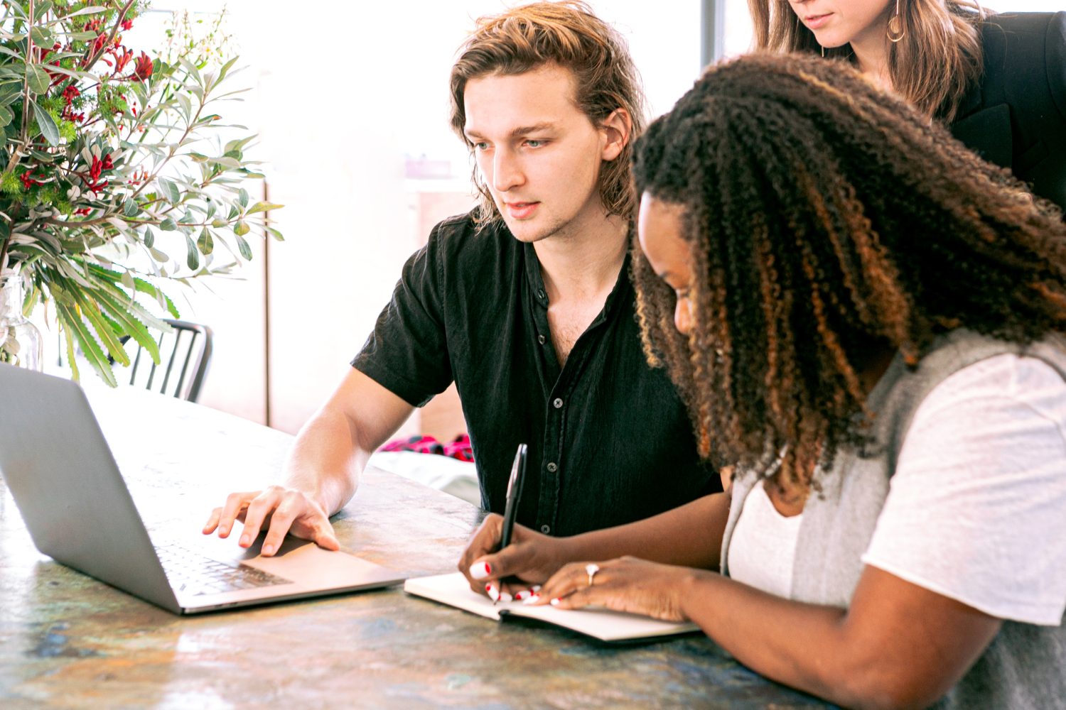 Three people gather around a laptop to work on a business plan