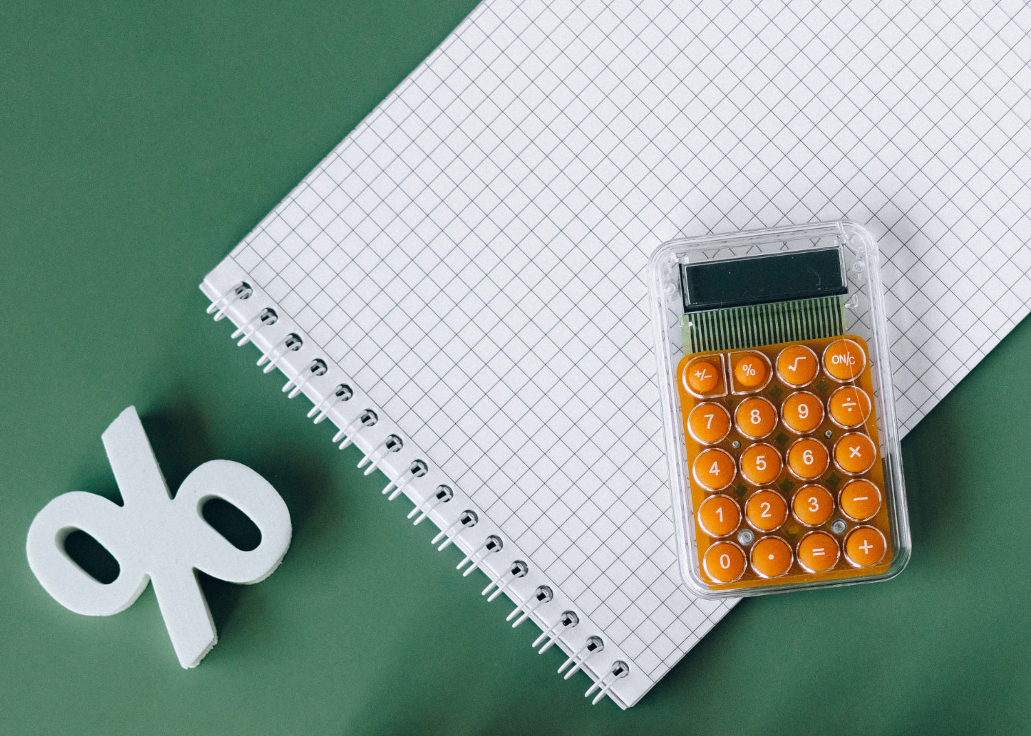 A calculator and a percentage sign on a table with a graphic paper pad