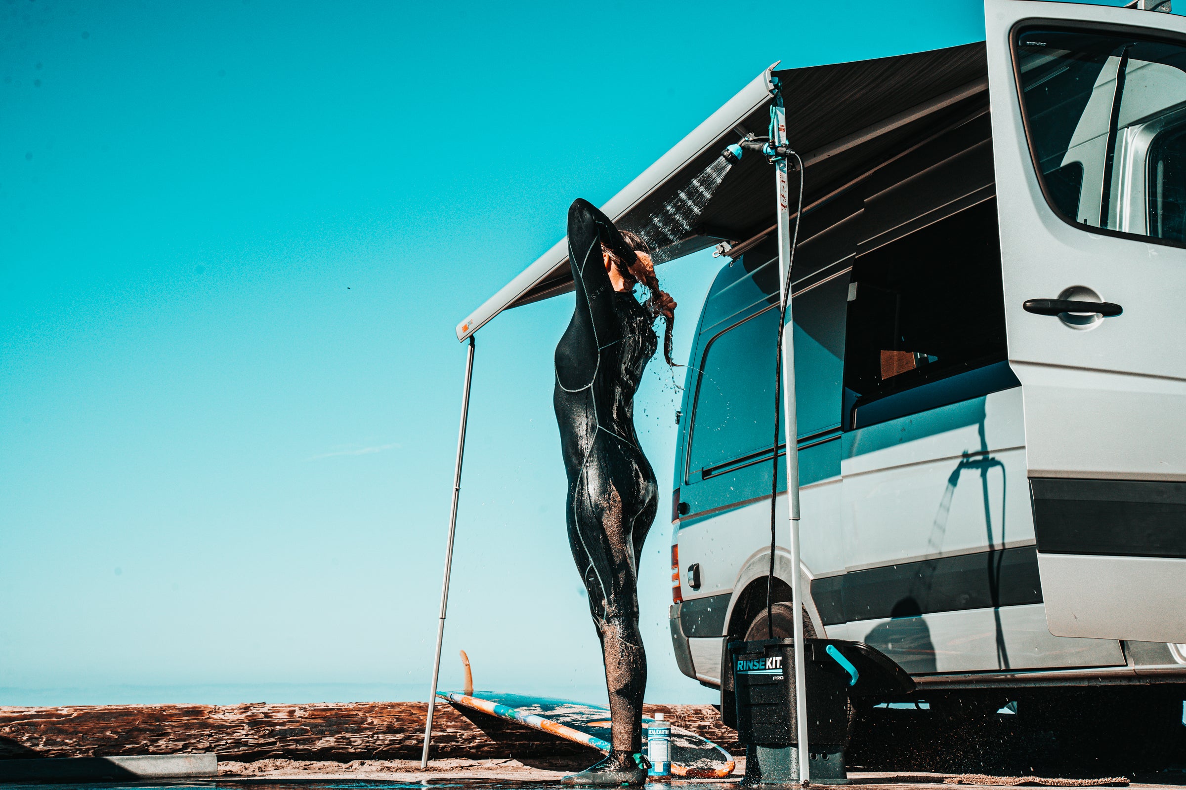 A surfer using a portable shower by RinseKit next to a camper van 