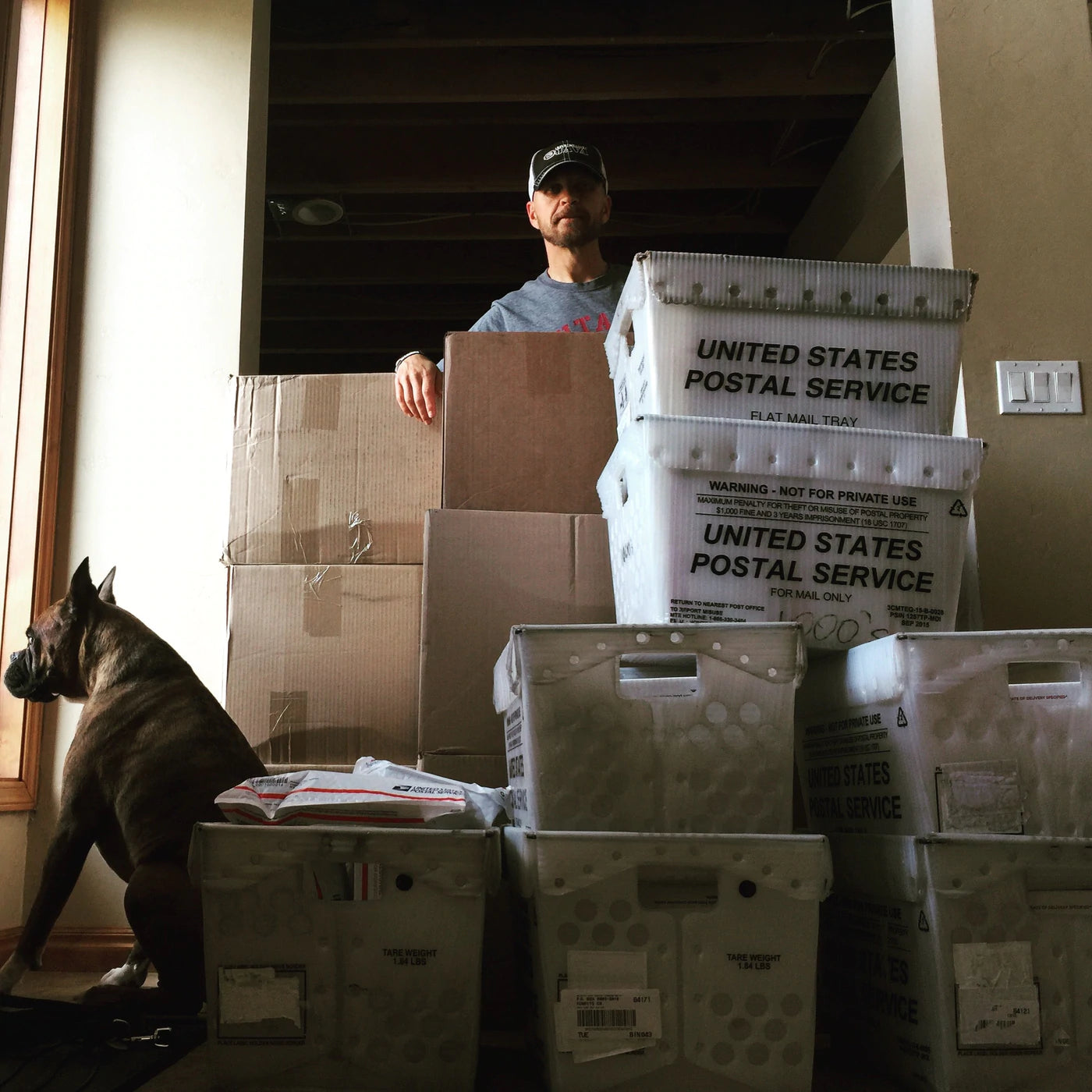 Carl Churchill poses with large coffee shipment boxes. A dog peers out a window beside him