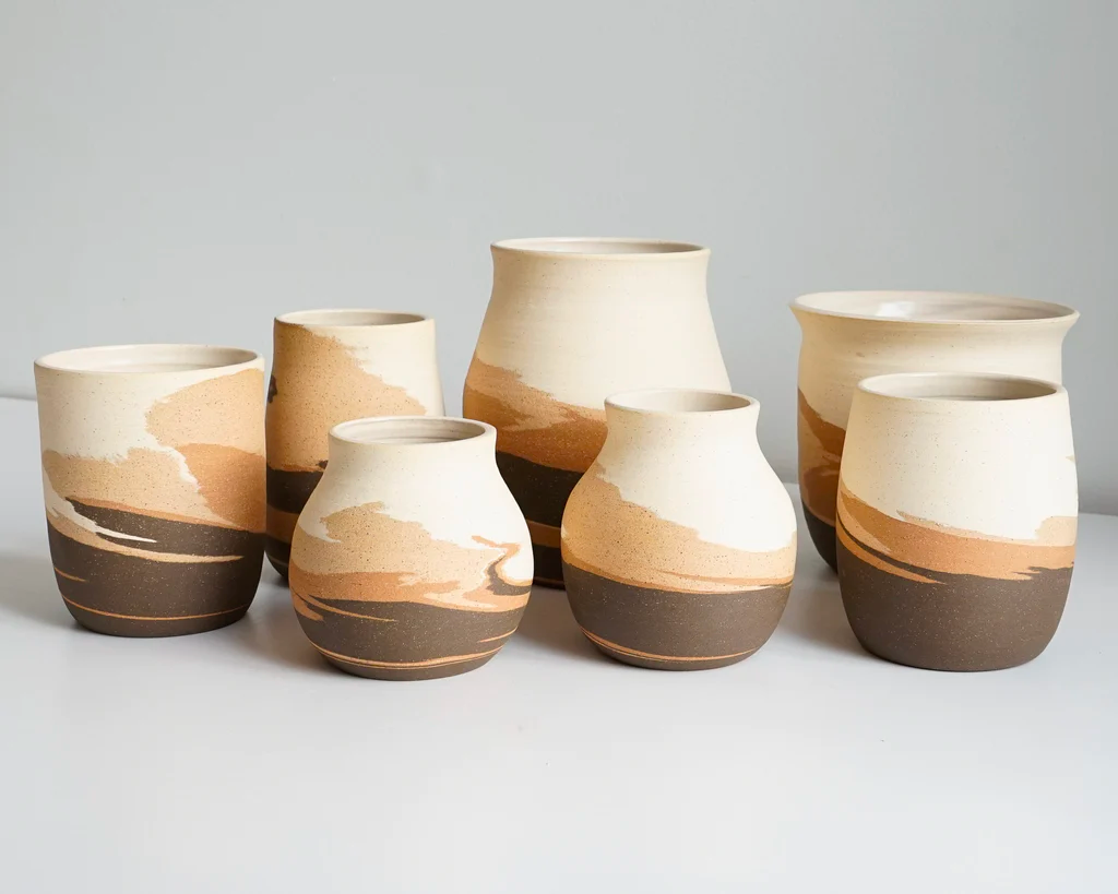 Ceramic vases with a rustic design in earth tones exhibited on a white surface.