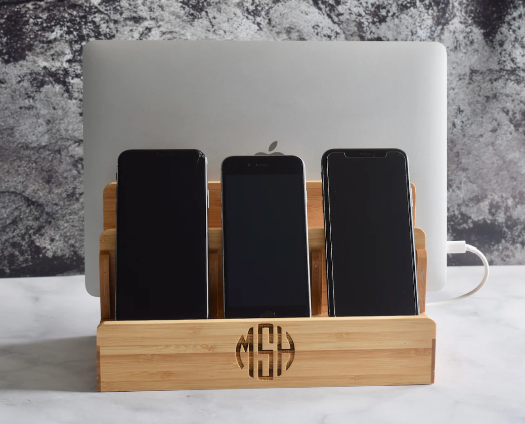 Three smartphones in a wooden charging station with a laptop in the background.