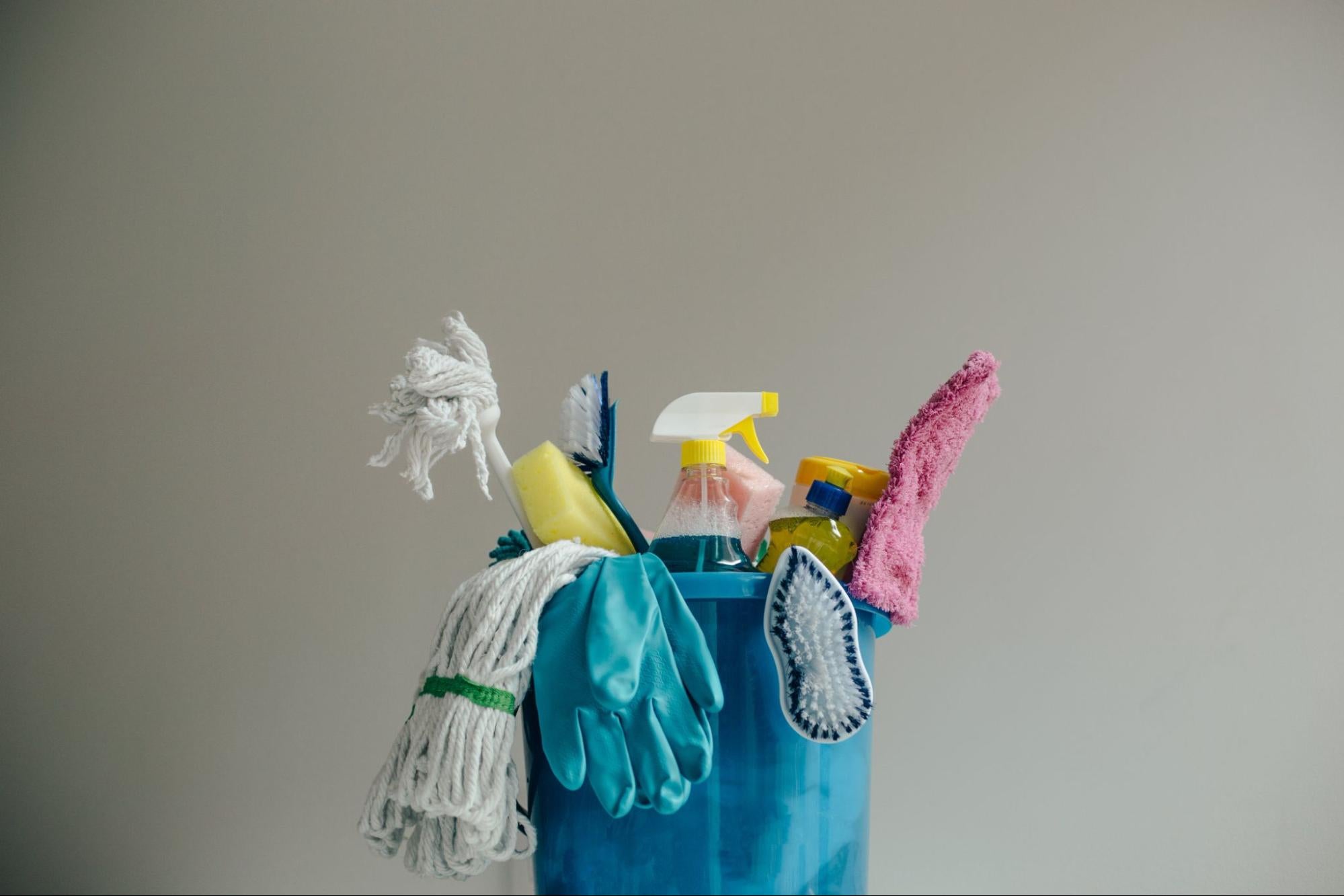 A bucket of cleaning supplies against a gray background.