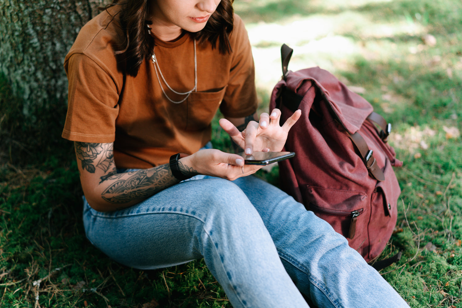 A person leans against a tree checking their mobile phone