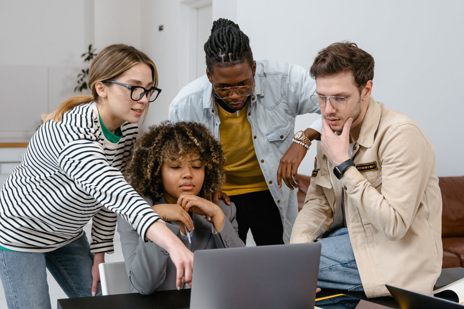 Four people lean over a laptop discussing a project