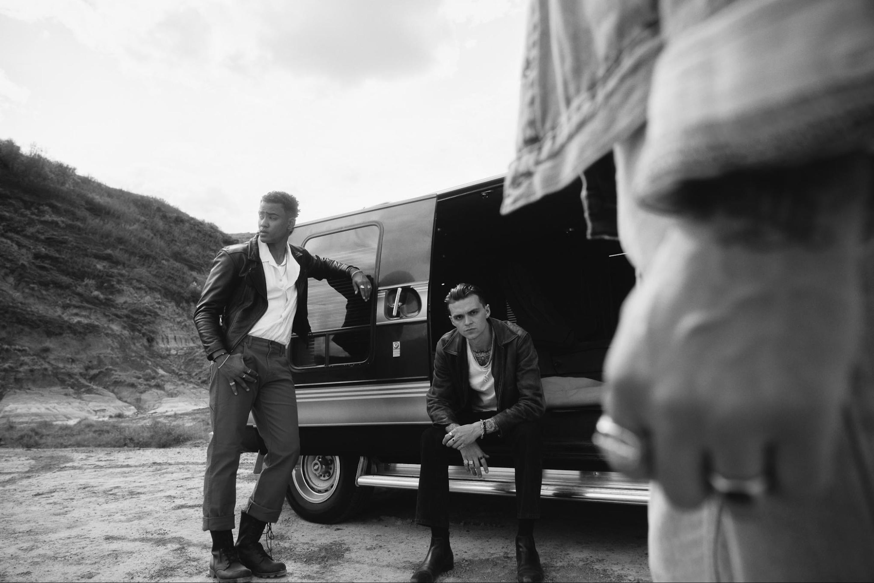 Greyscale photo of three men standing in the desert in front of a caravan with Clocks and Colours rings and bracelets on their hands.