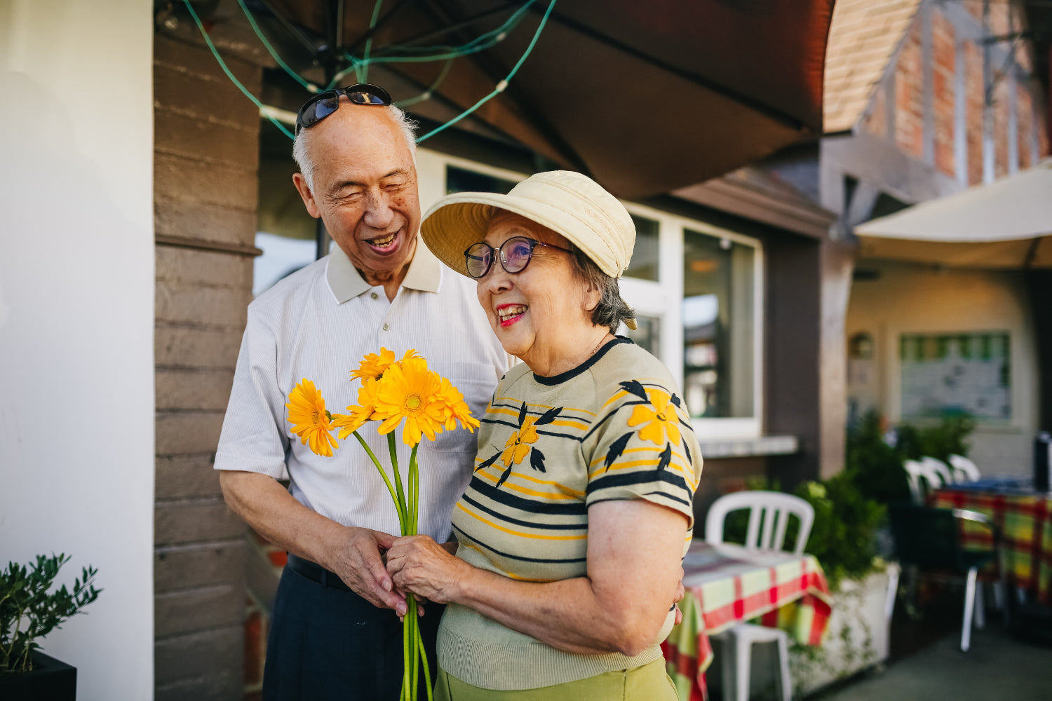 Two older people walk on a sidewalk with one holding flowers