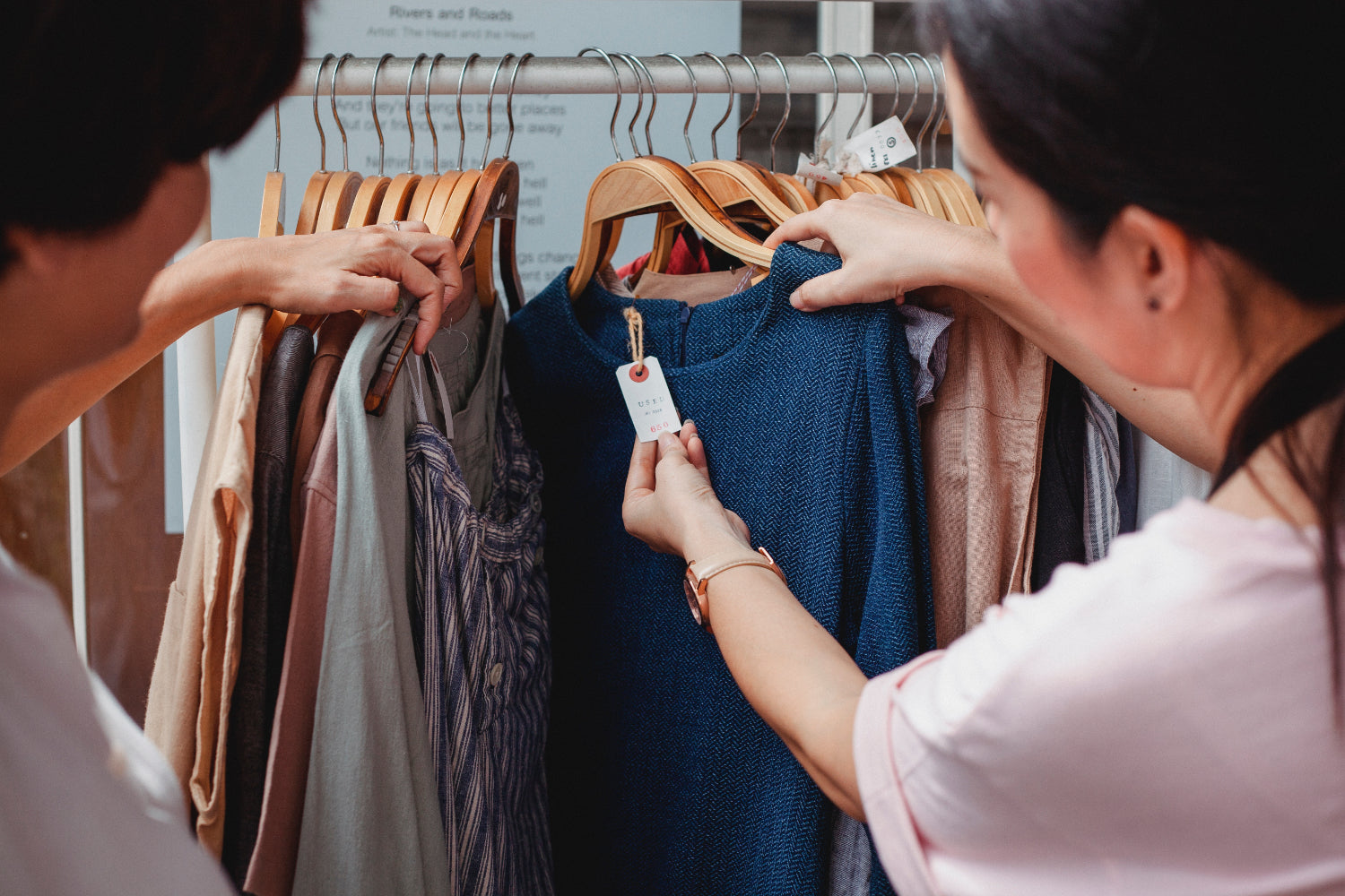 Two people look through a rack of clothes and examine the tags
