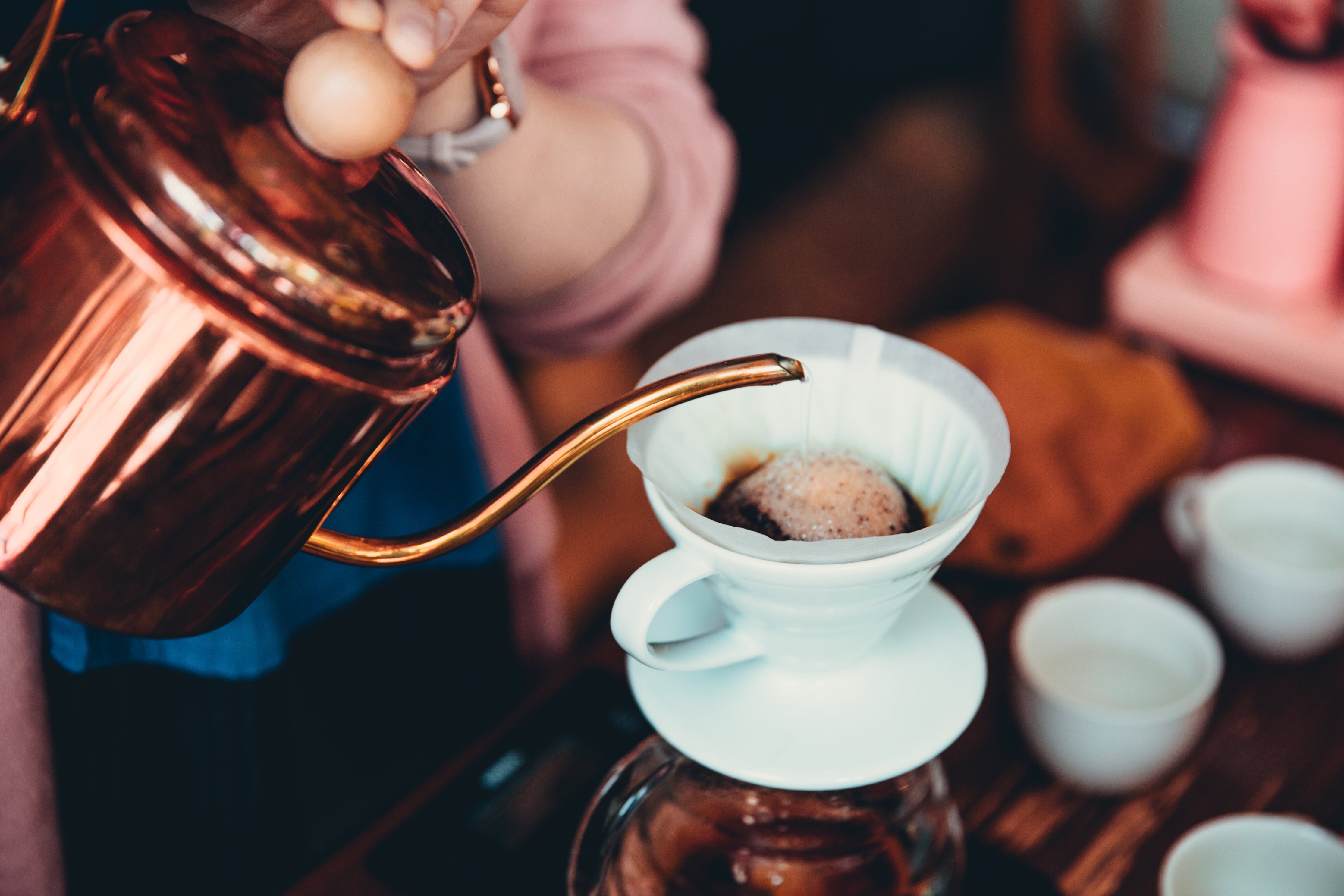 Imagem de estilo de vida de uma mão despejando água de uma chaleira de cobre em uma cafeteira
