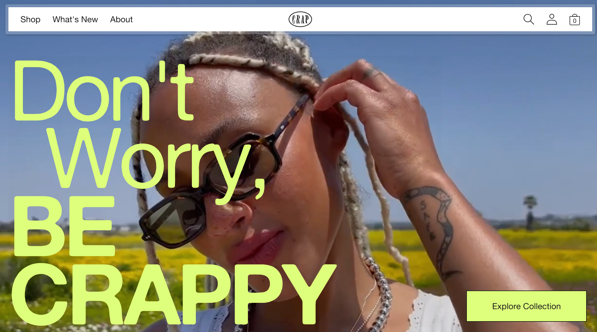 A woman wearing sunglasses tucks her hair behind her ear in front of blue skies and green fields.