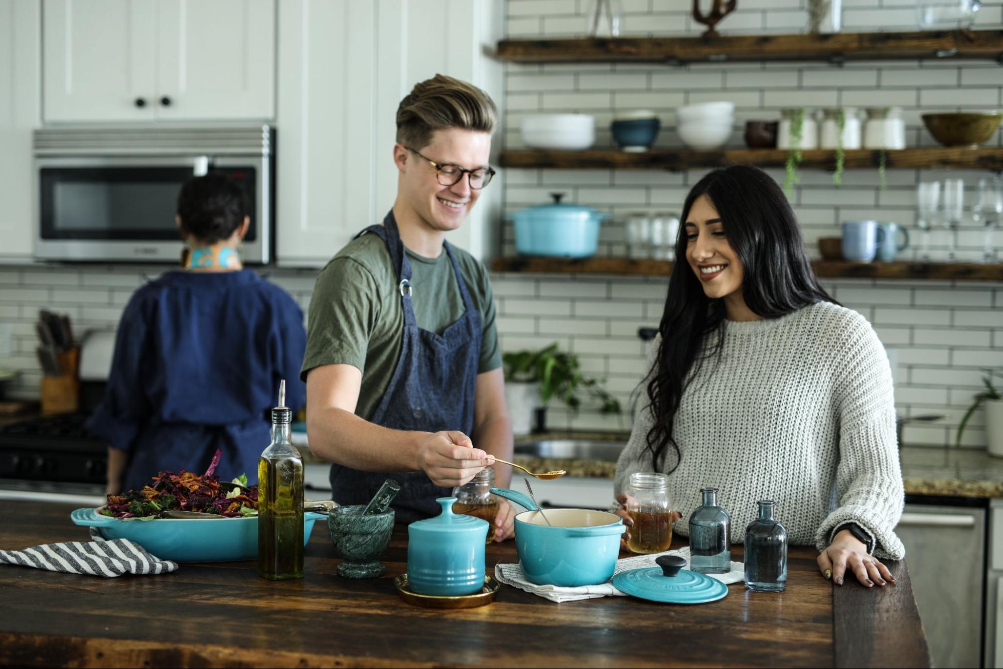 Two people standing at a kitchen island learning how to cook with creuset kitchenware nearby