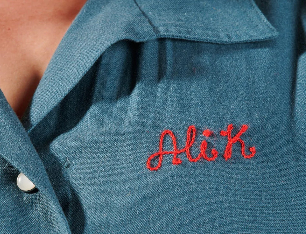 Close up of a shirt lapel featuring a custom embroidered name tag reading "Ali K."