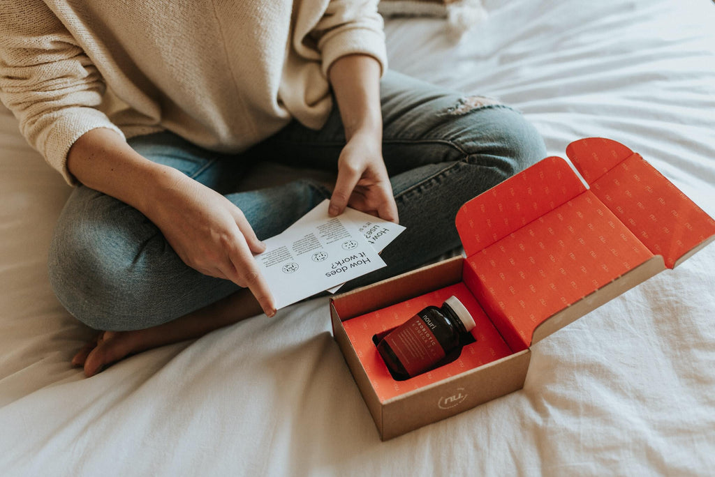 每天nouri/Unsplash -一个女人坐在床上看着卡片，卡片上有一个装在盒子里的益生菌礼物-影响者的礼物